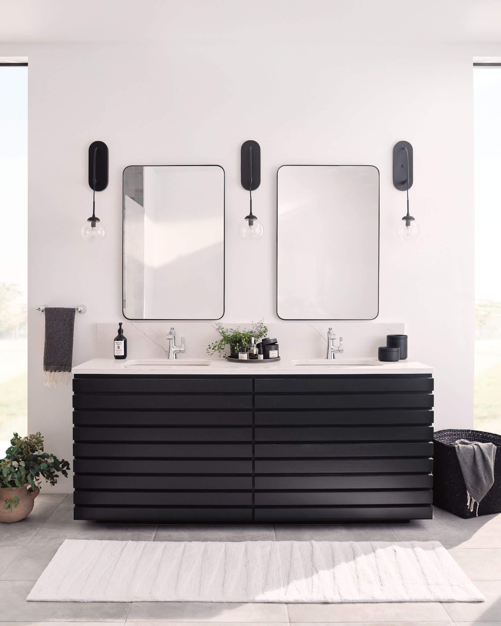 Chrome single-handle bathroom sink faucet with curved spout mounted on white countertop between two rectangular mirrors.