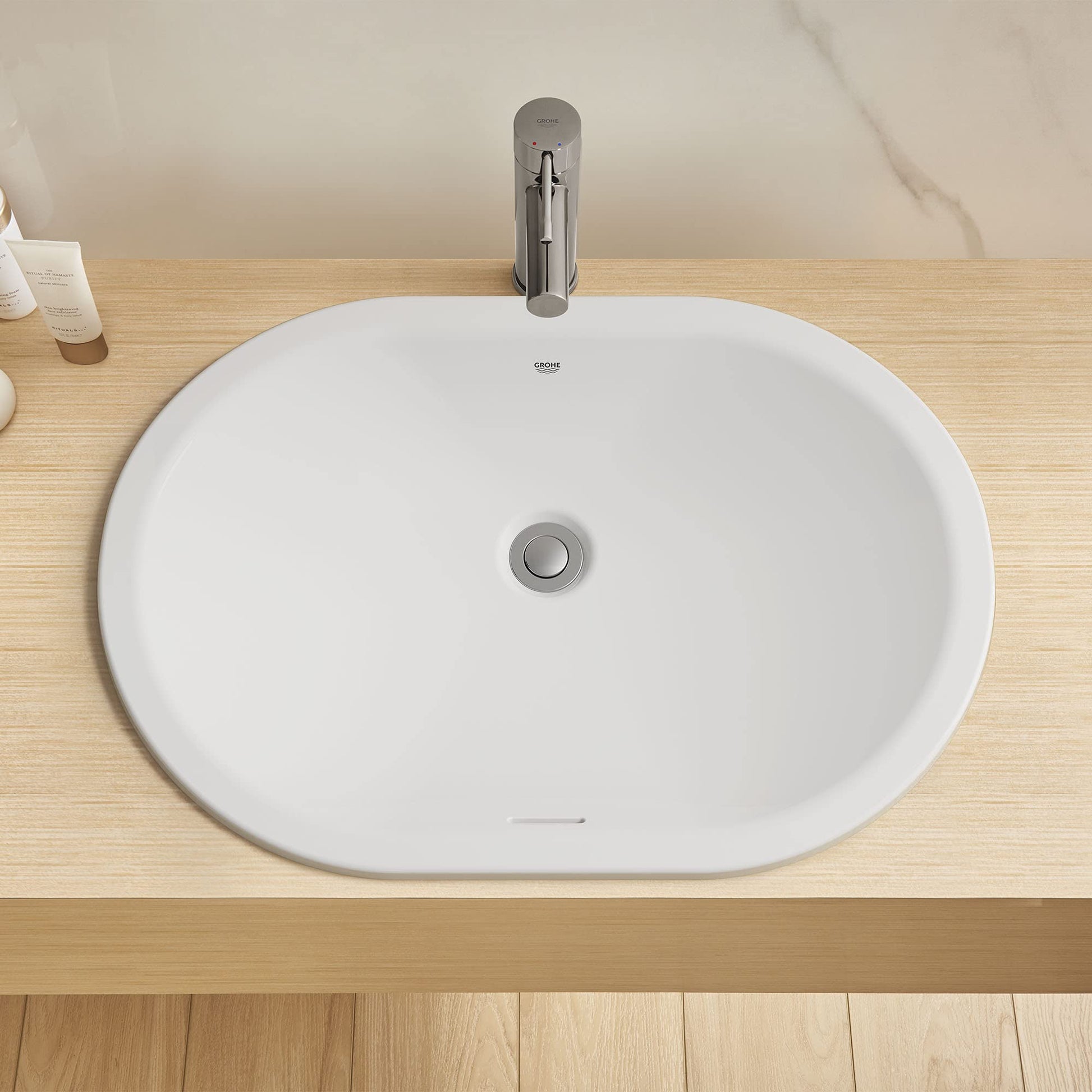 White oval undermount bathroom sink with chrome drain and faucet on wooden countertop.