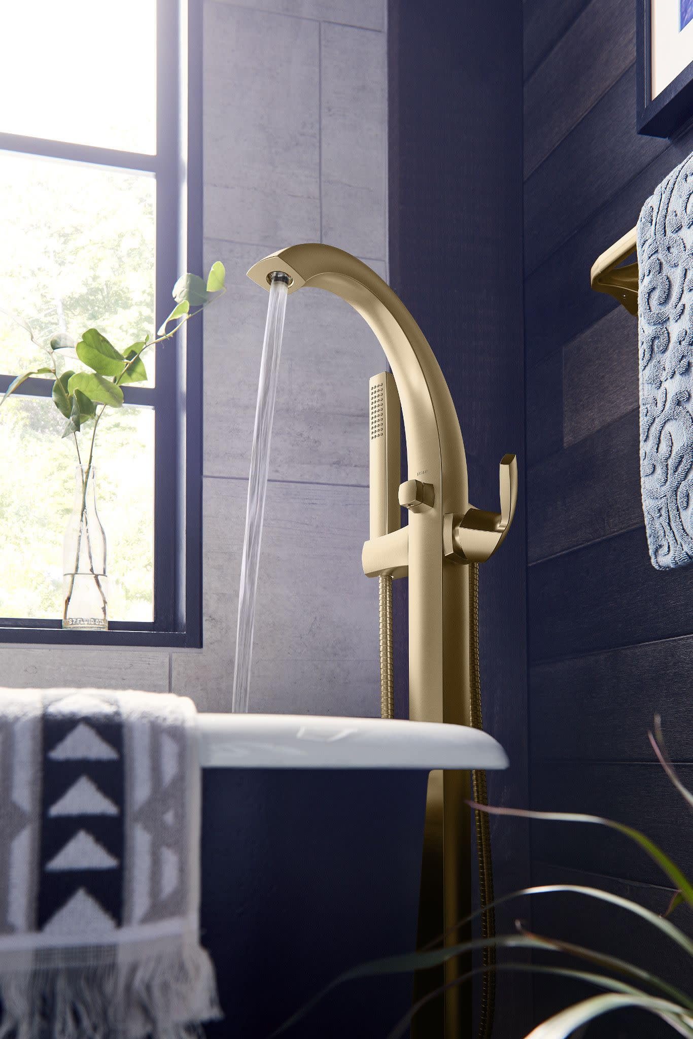 Brushed gold freestanding tub filler with curved spout, single handle, and detachable handheld showerhead.