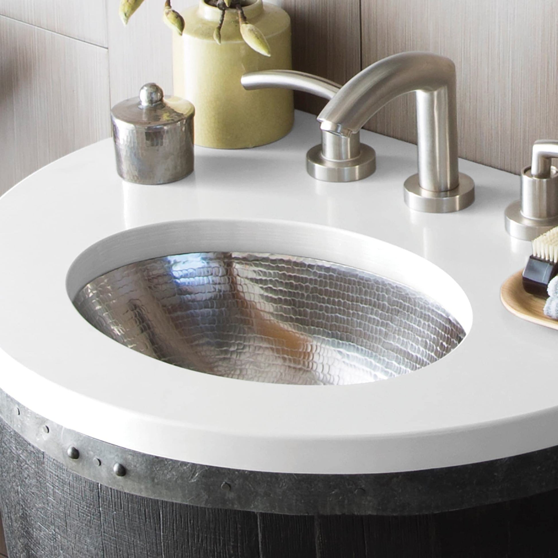 Polished nickel faucet with curved spout mounted above hammered metal oval sink basin.