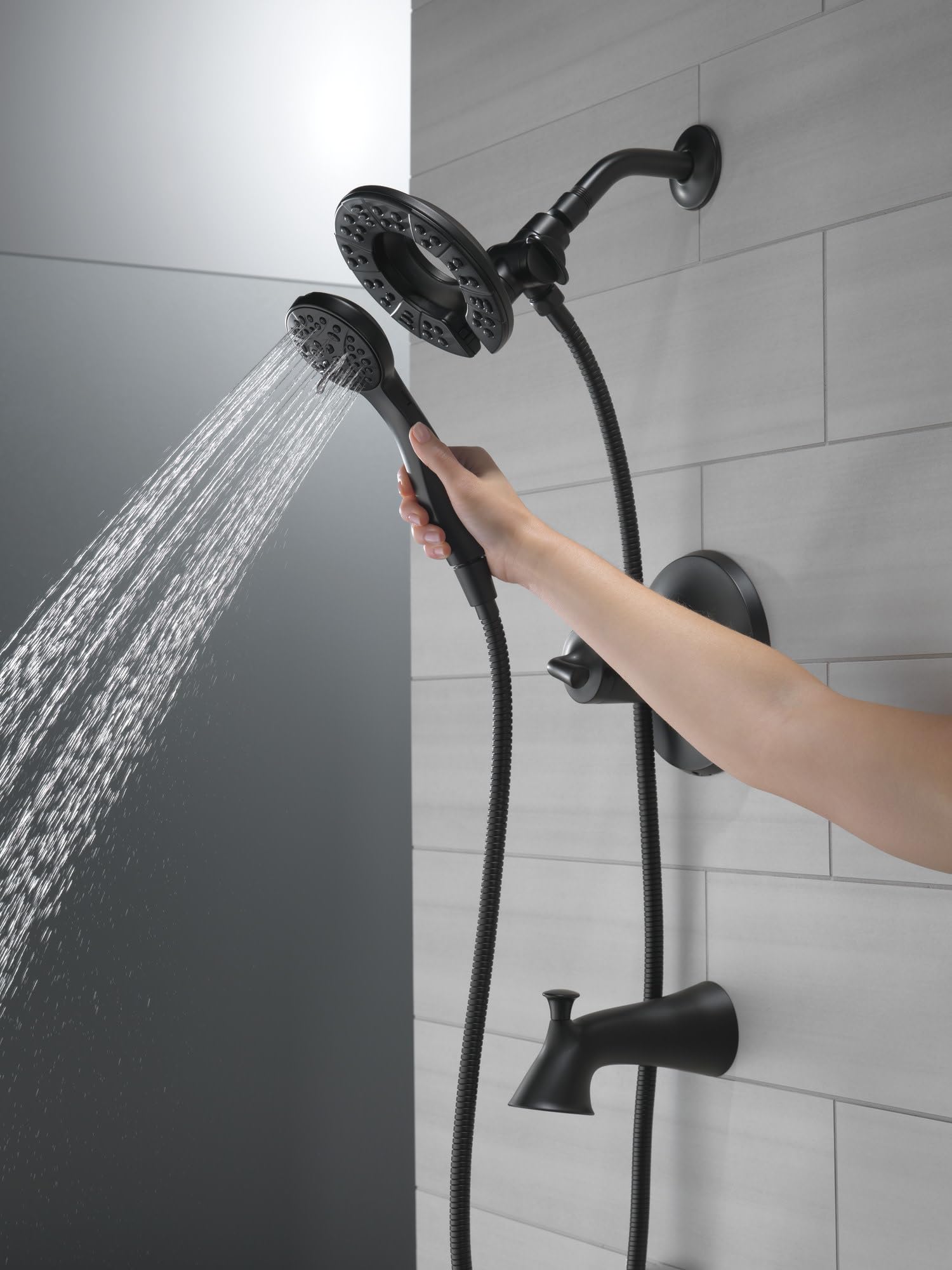 Black tub and shower trim with dual showerheads, handheld wand, and spout mounted on tile wall.