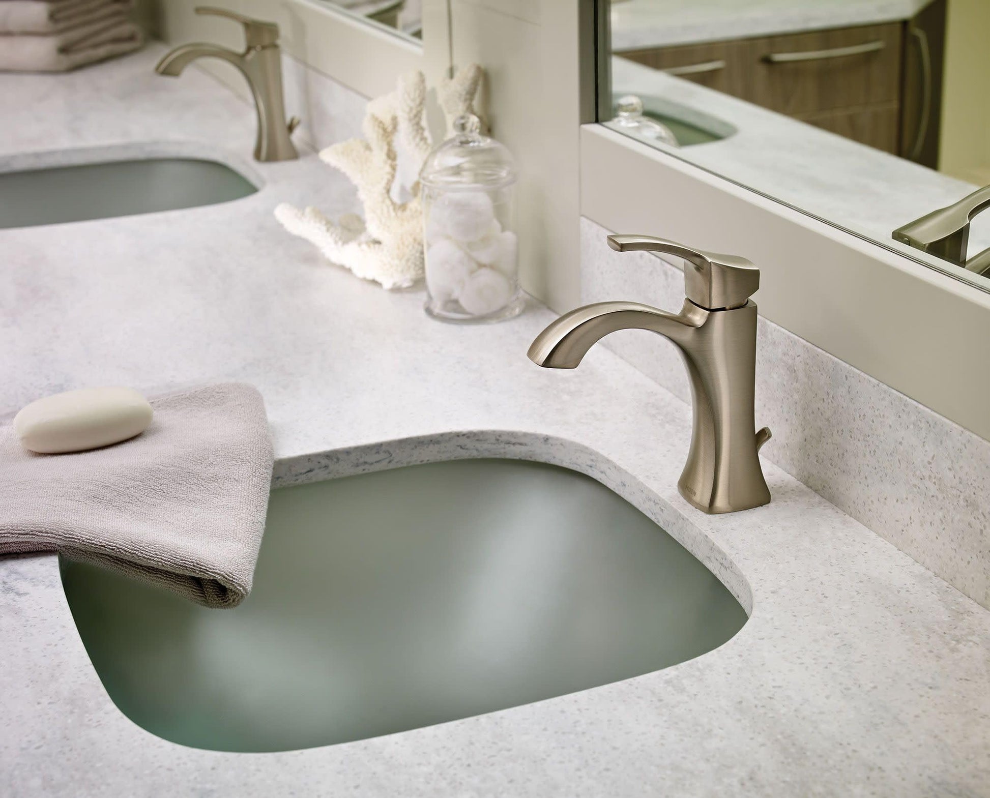 Brushed nickel single-handle bathroom faucet with high arc spout mounted on white marble countertop above sink.