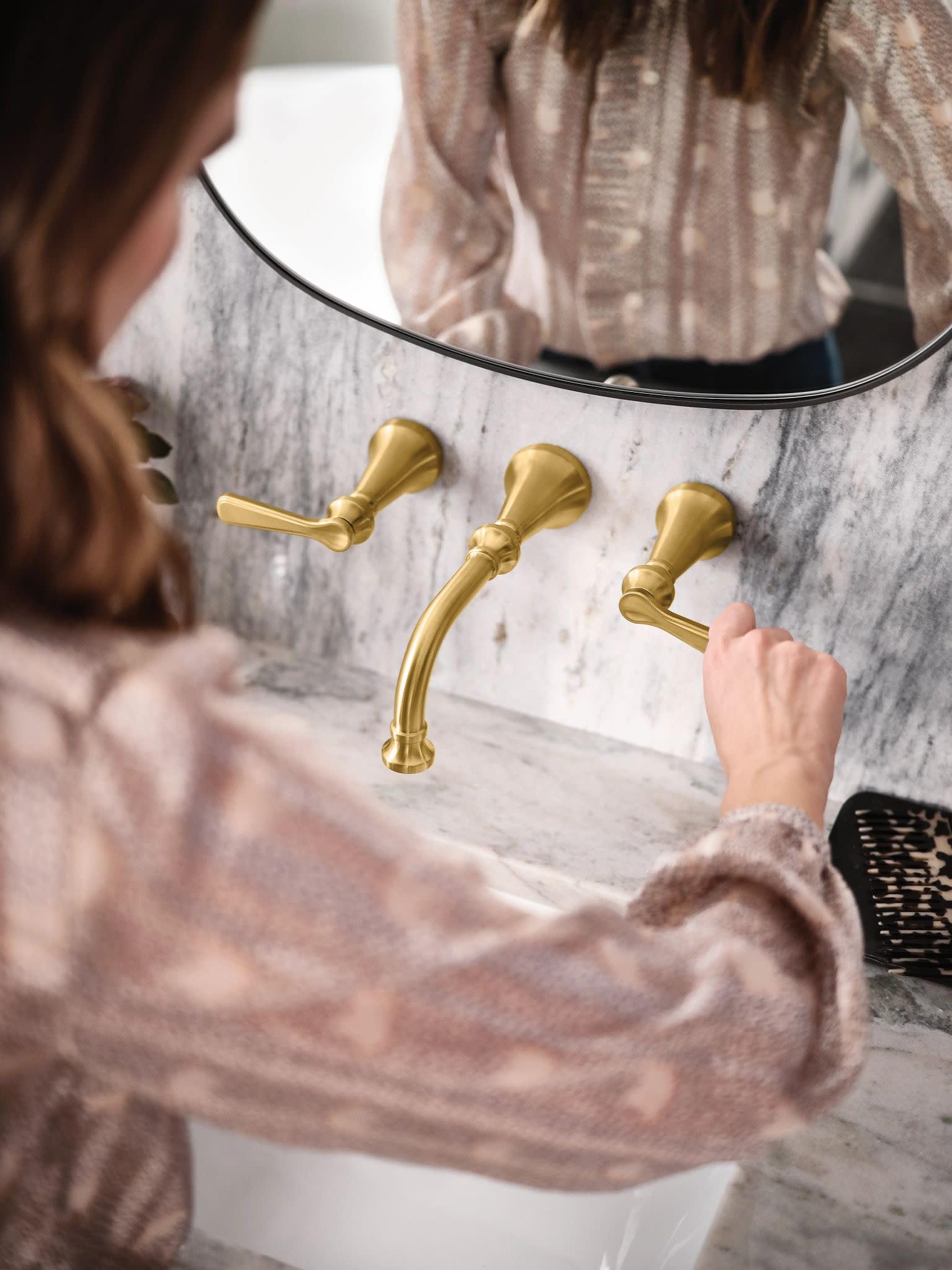 Brushed gold widespread bathroom faucet with traditional lever handles mounted on marble sink surround.