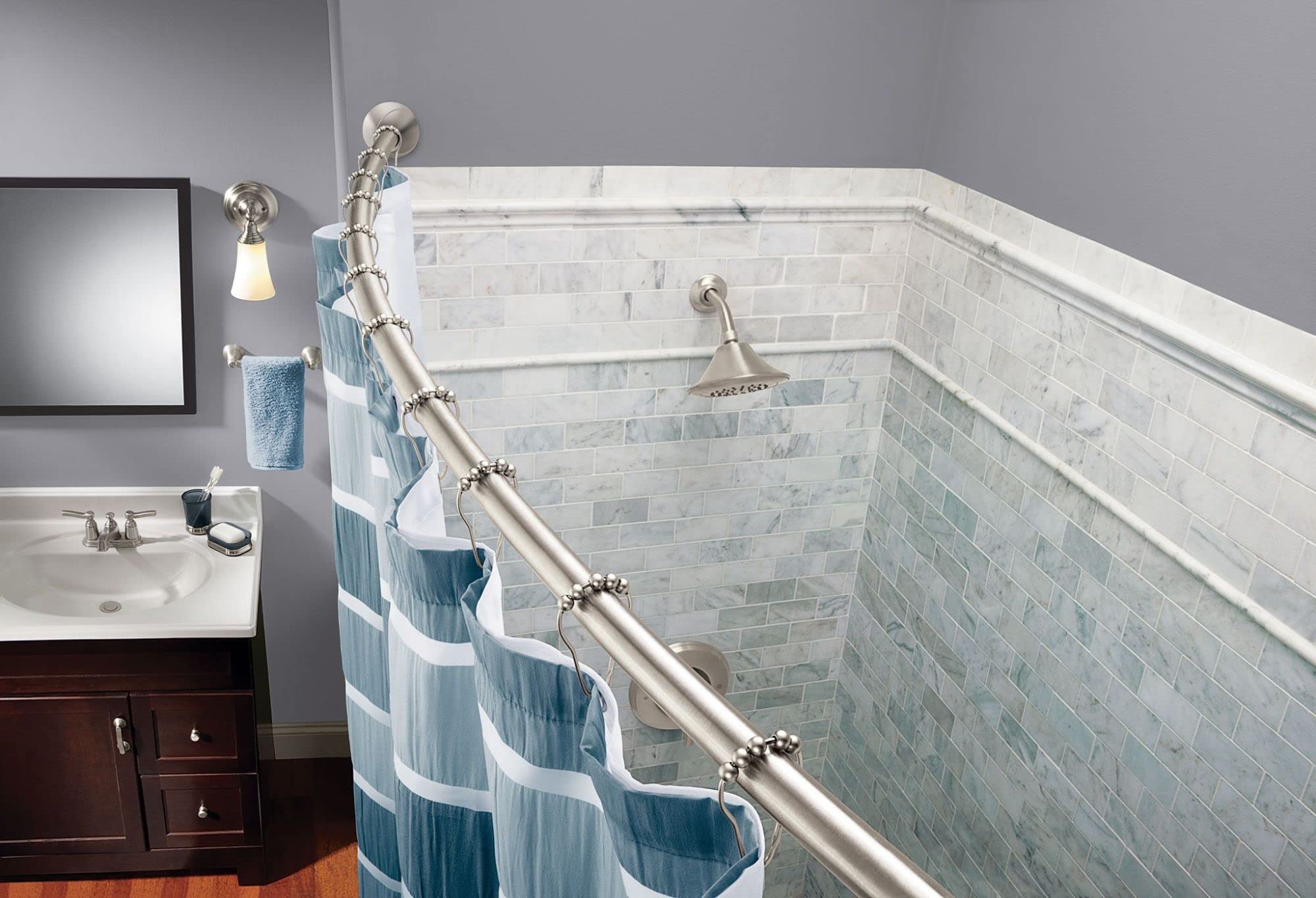 Brushed nickel curved shower curtain rod installed in bathtub enclosure with blue and white patterned curtain.