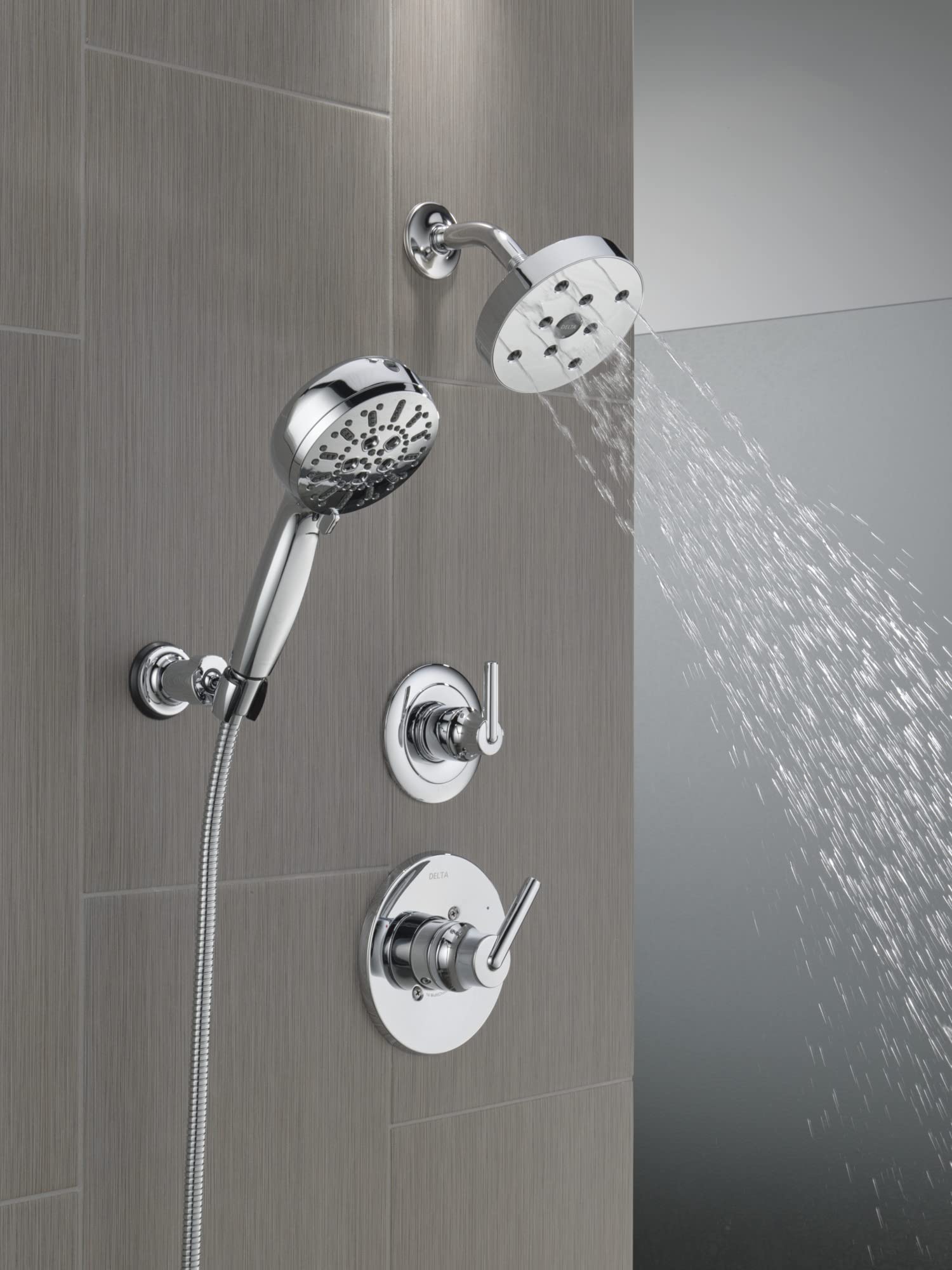 Chrome wall-mounted shower system with fixed showerhead, handheld sprayer on hose, and dual control valves installed on tile 