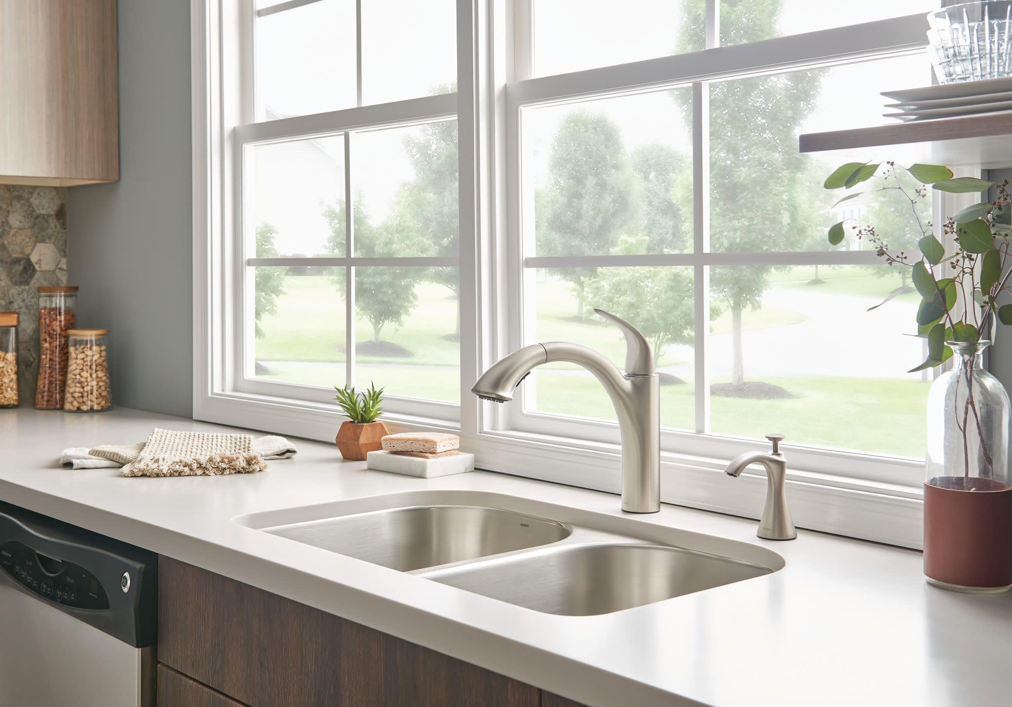 Stainless steel kitchen faucet with single handle and pullout spray head installed above double sink at kitchen window.