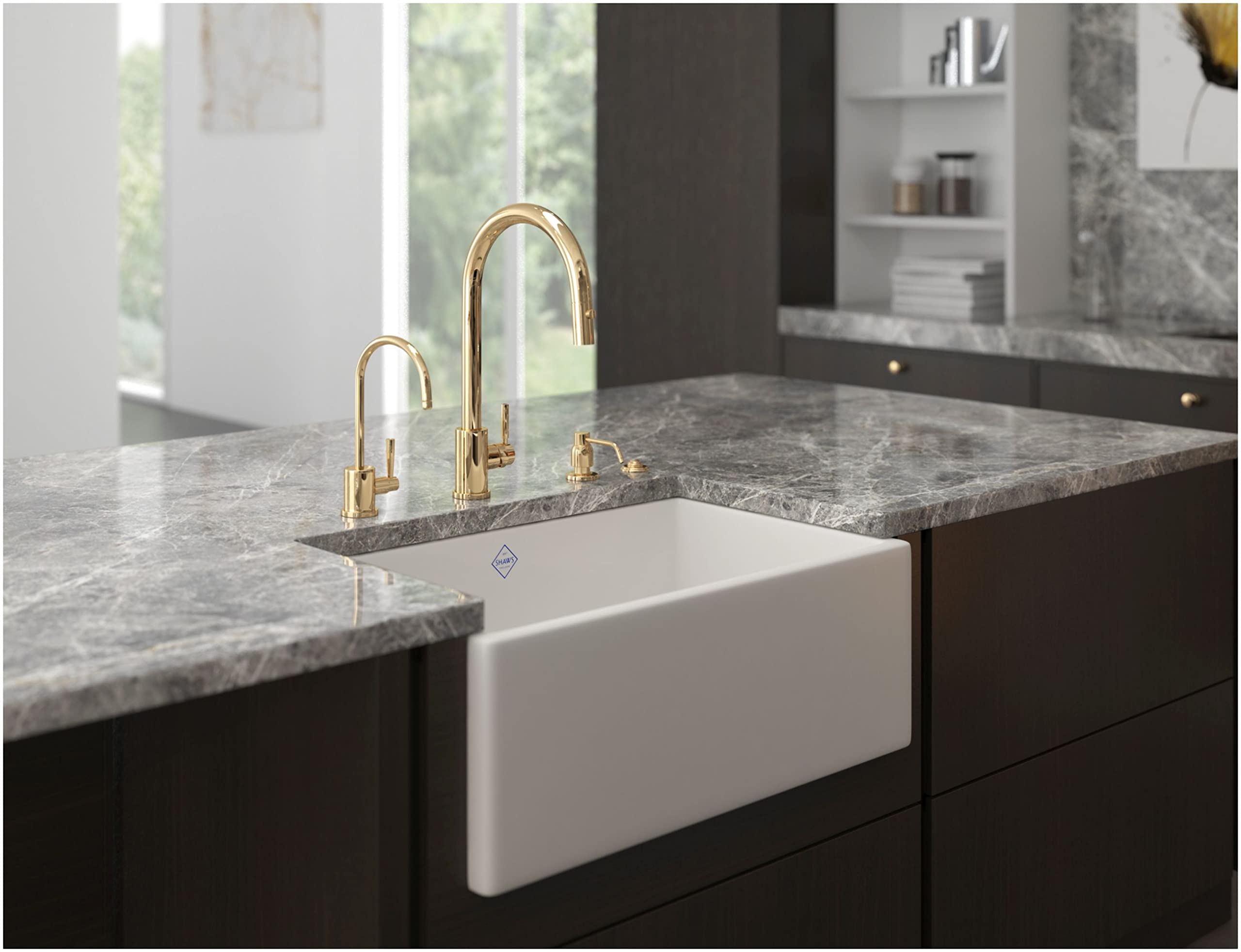 Satin English gold kitchen faucet with curved spout mounted above white apron-front sink in gray countertop.