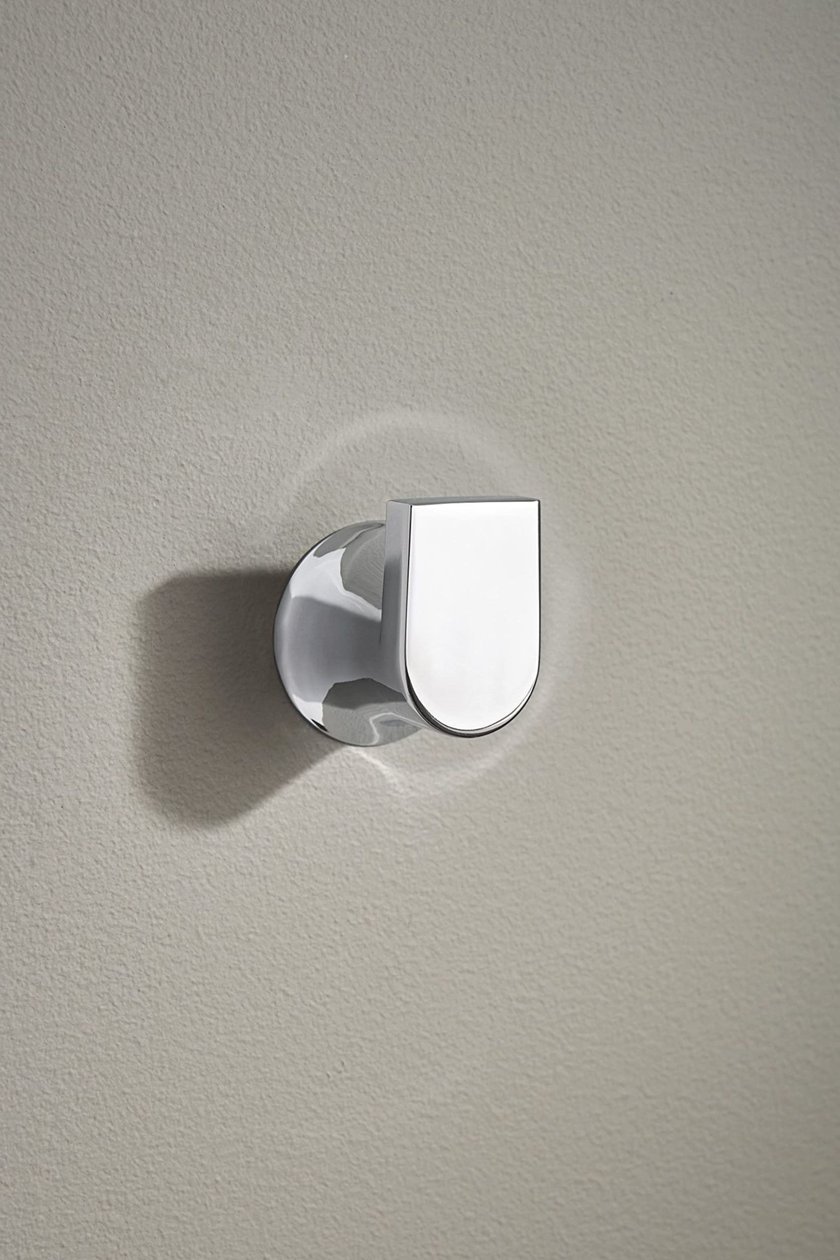 Chrome wall-mounted robe hook with rounded rectangular hook and circular mounting plate on white textured wall.