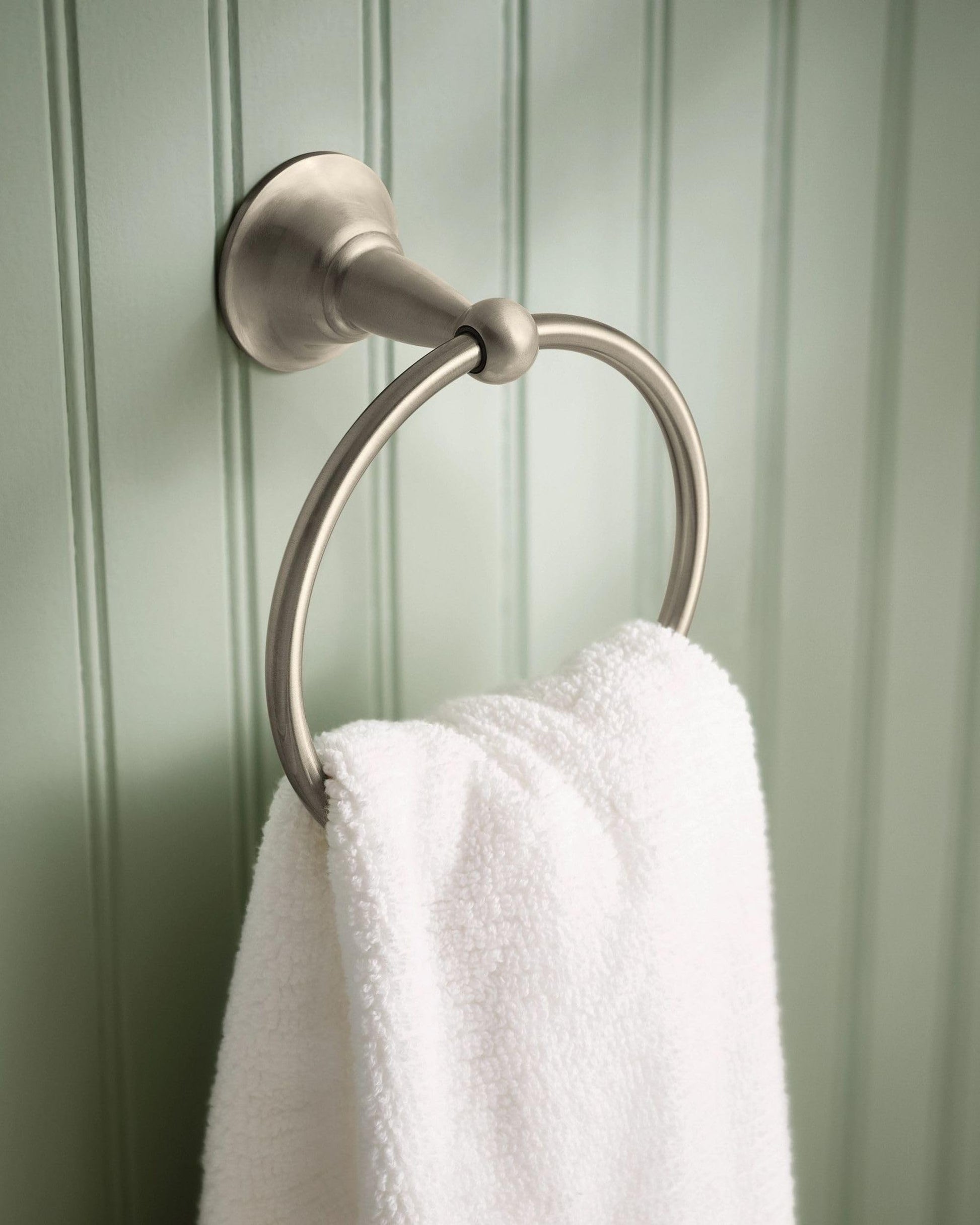 Brushed nickel wall-mounted towel ring with circular design holding a white towel against green paneled wall.