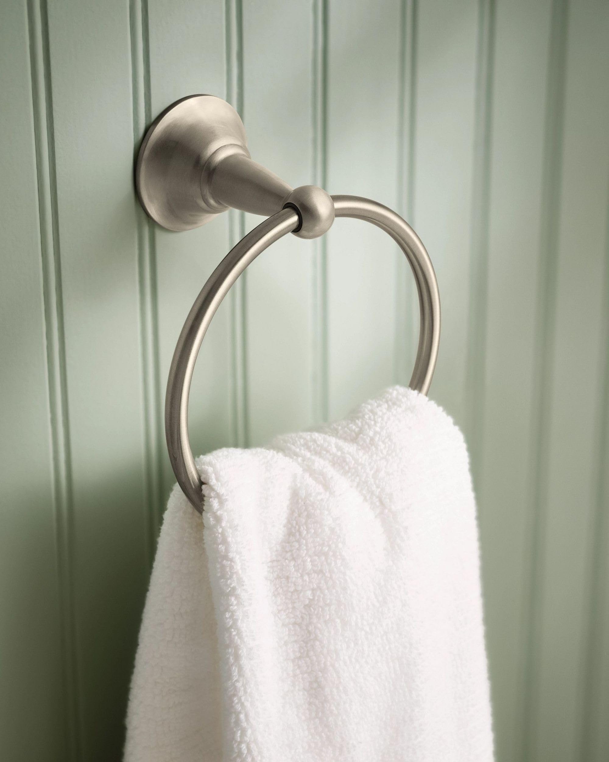 Brushed nickel wall-mounted towel ring with circular design holding a white towel against green paneled wall.