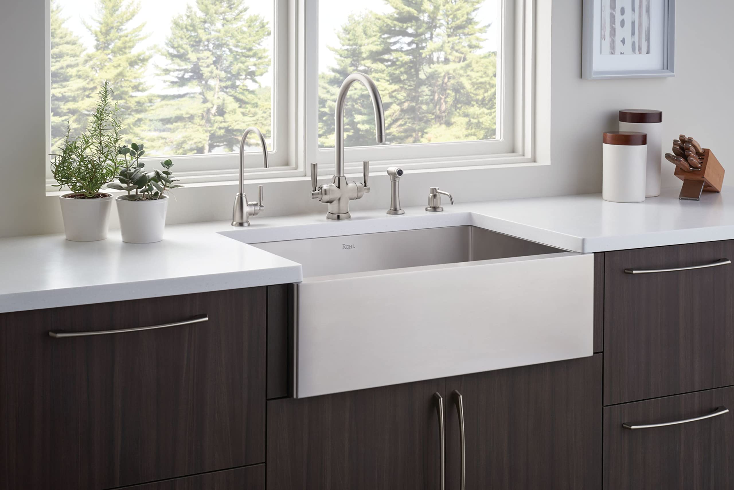 Satin English Gold hot water dispenser with curved spout mounted on white kitchen sink countertop beside farmhouse sink.