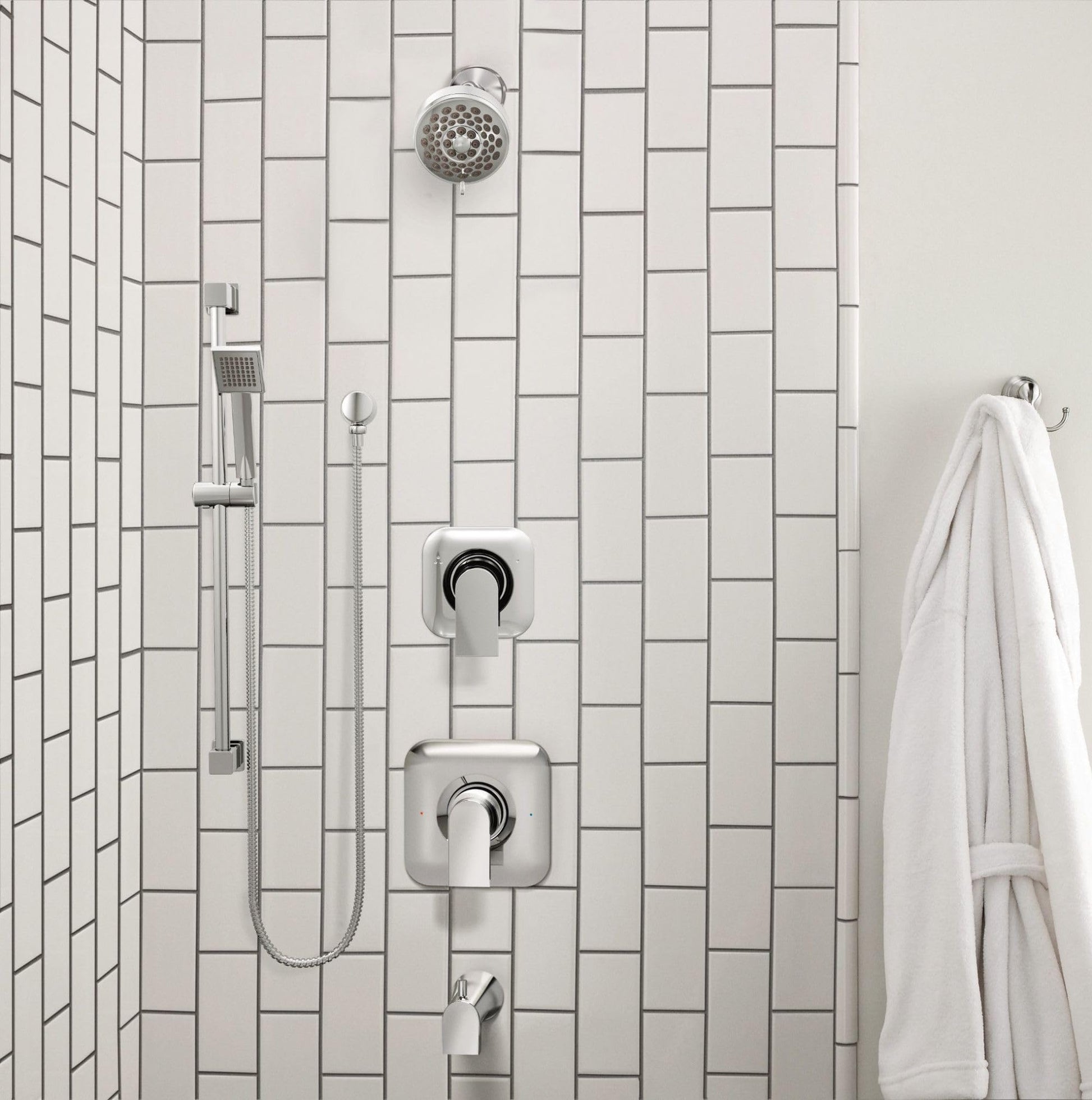 Chrome handheld showerhead with slide bar, metal hose, and dual wall-mounted controls on subway tile background.