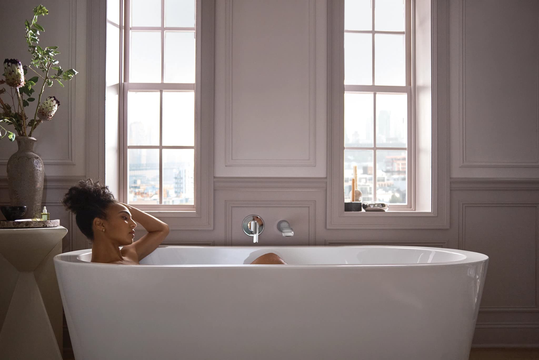Chrome wall-mounted tub faucet with single handle and extended spout installed above white freestanding bathtub.