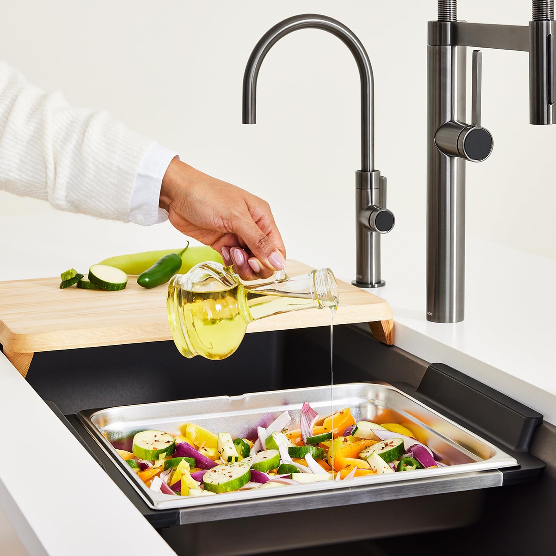 Stainless steel rectangular sink tray filled with chopped vegetables, positioned in black sink basin below kitchen faucet.