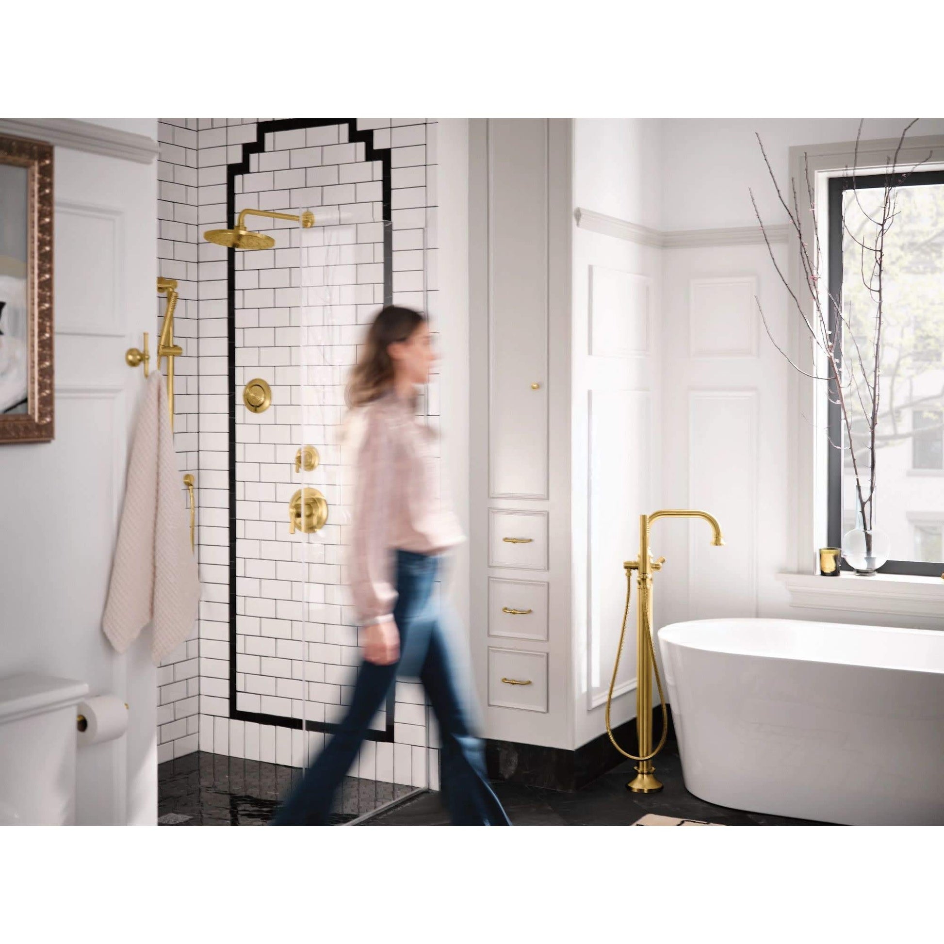 Matte black freestanding floor mount tub filler with single handle and handheld showerhead next to white freestanding bathtub