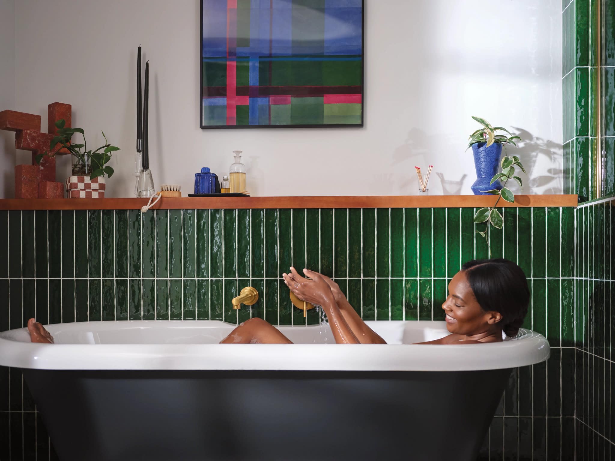 Brushed gold wall-mounted tub faucet with single handle and curved spout installed above black and white soaking tub.