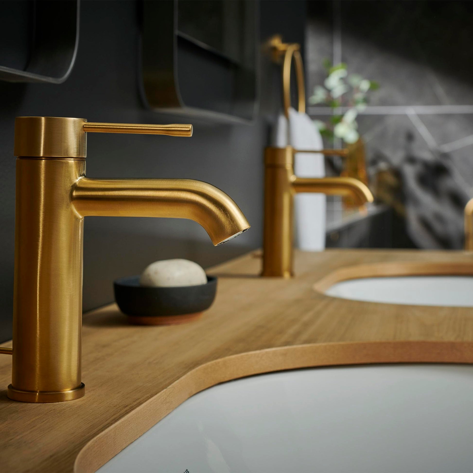 Brushed gold single-handle bathroom faucet with curved spout mounted on wooden vanity with white sink.