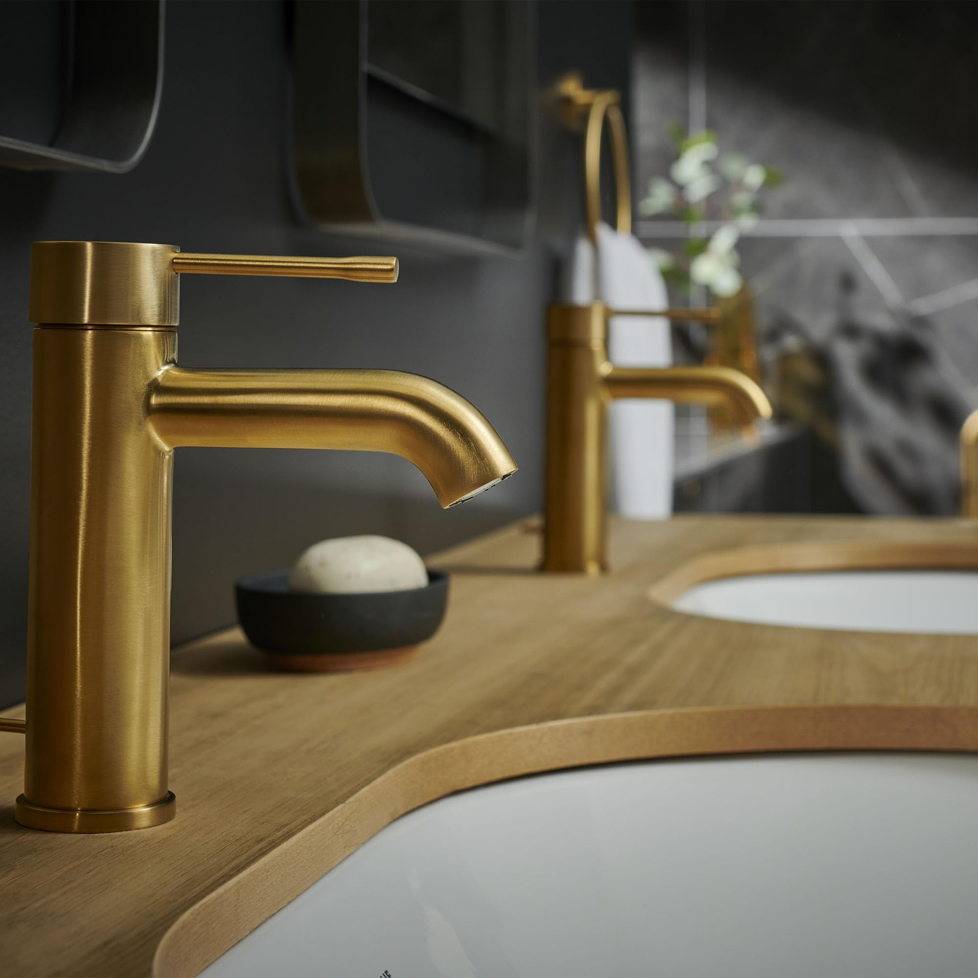 Brushed gold single-handle bathroom faucet with curved spout mounted on wooden vanity with white sink.