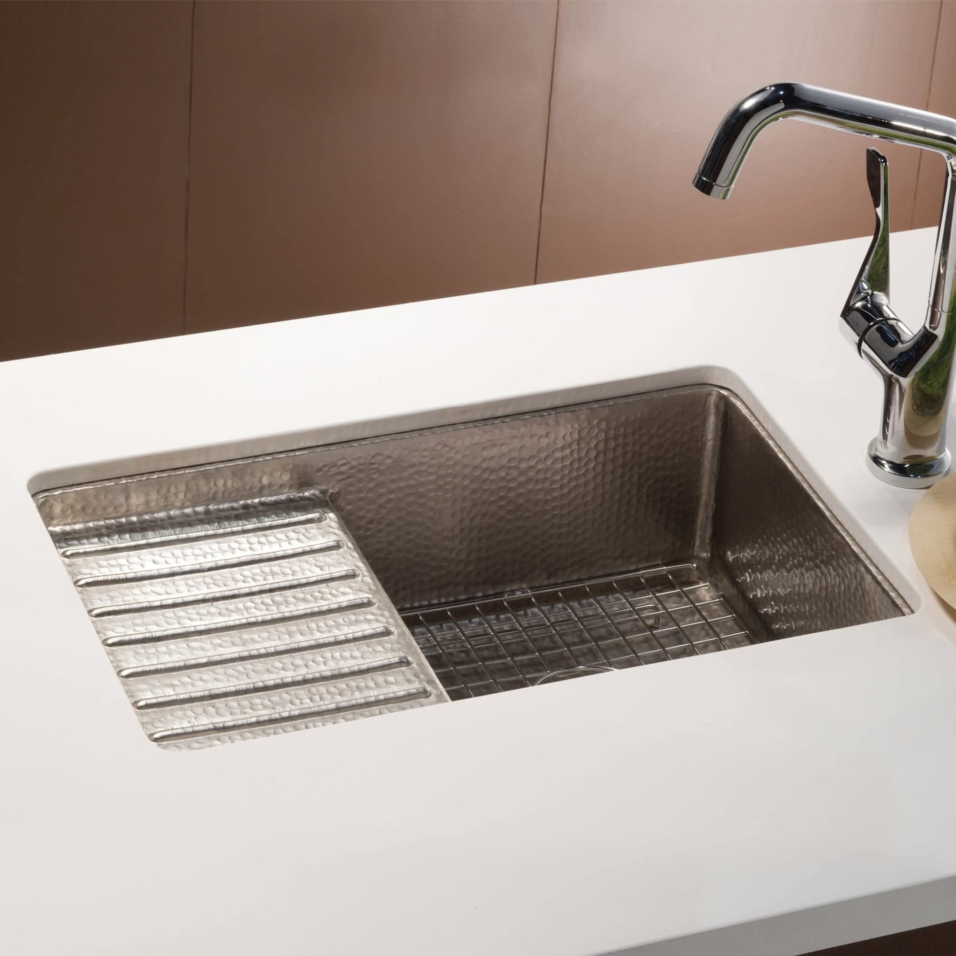 Hammered copper undermount sink with two compartments, drainboard, and chrome faucet installed in white countertop.