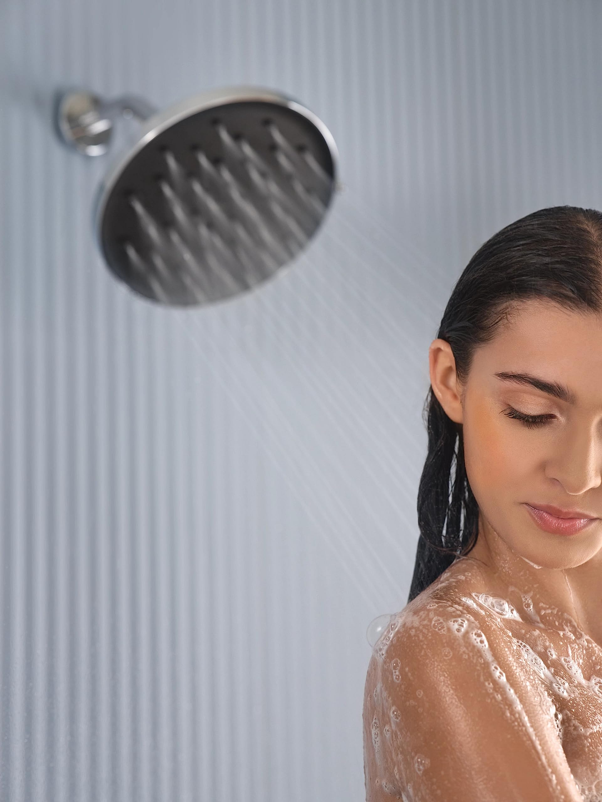 Chrome rainshower head with linear spray pattern mounted on wall above person showering.