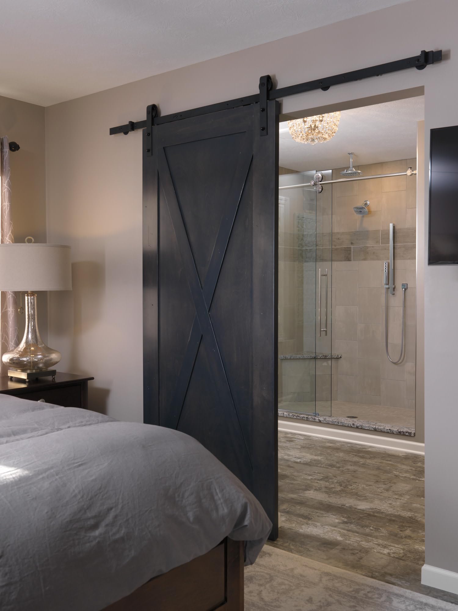 Stainless steel shower arm and flange mounted to ceiling above glass-enclosed shower enclosure.