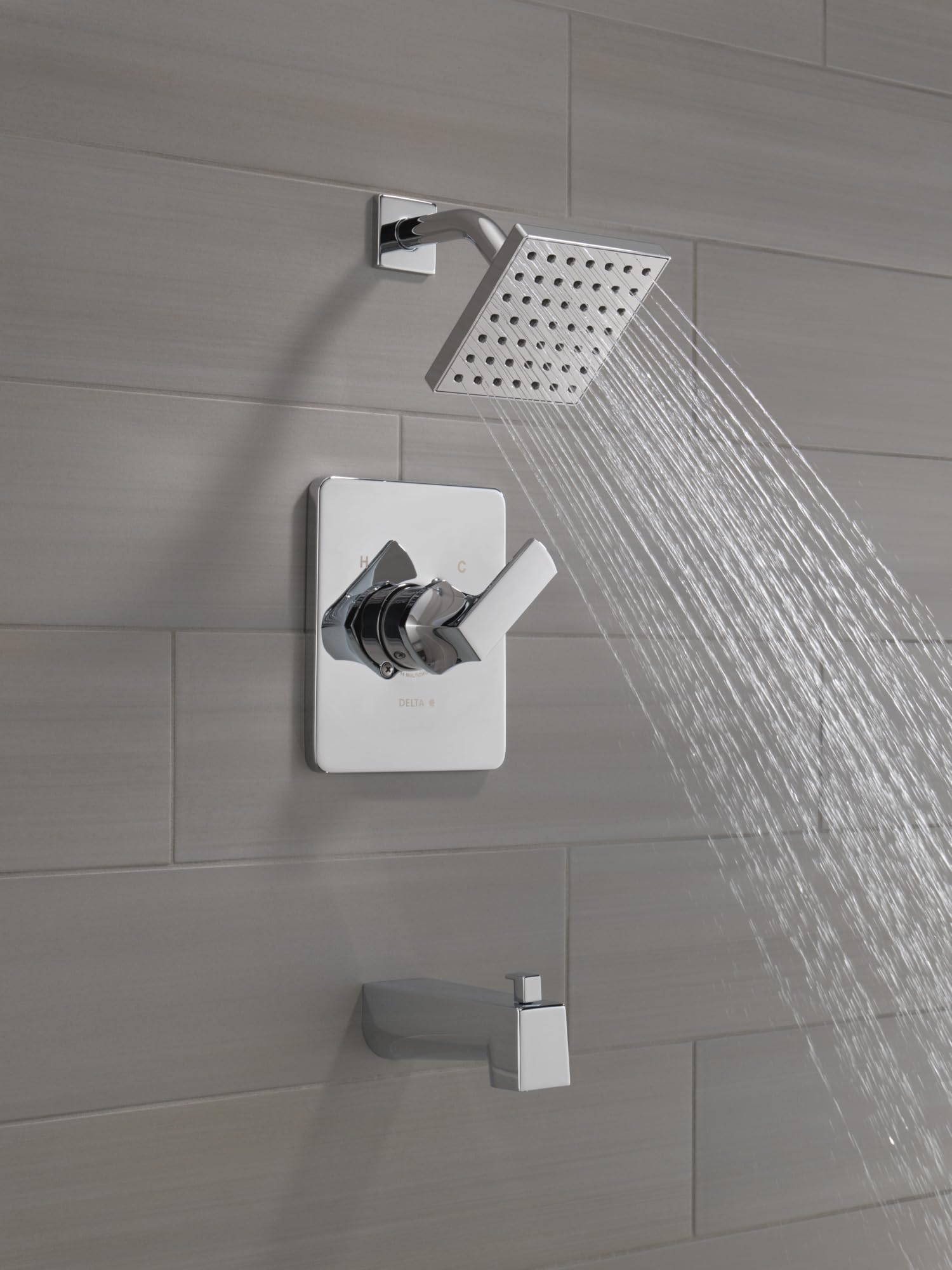 Chrome tub and shower system with square showerhead, wall-mounted valve control, and tub spout on tiled bathroom wall.