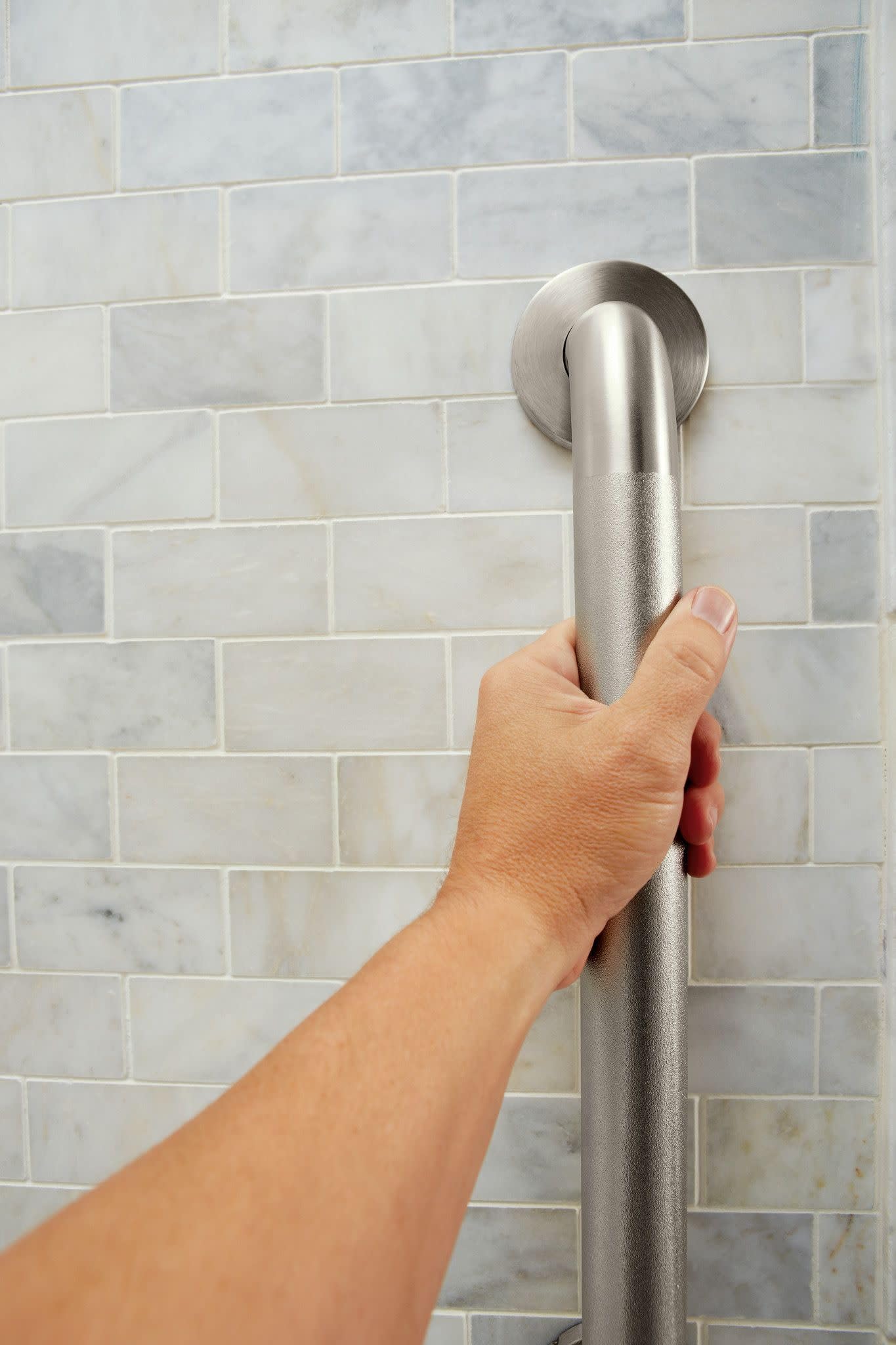 Brushed stainless steel grab bar mounted horizontally on subway tile wall with hand gripping for demonstration.