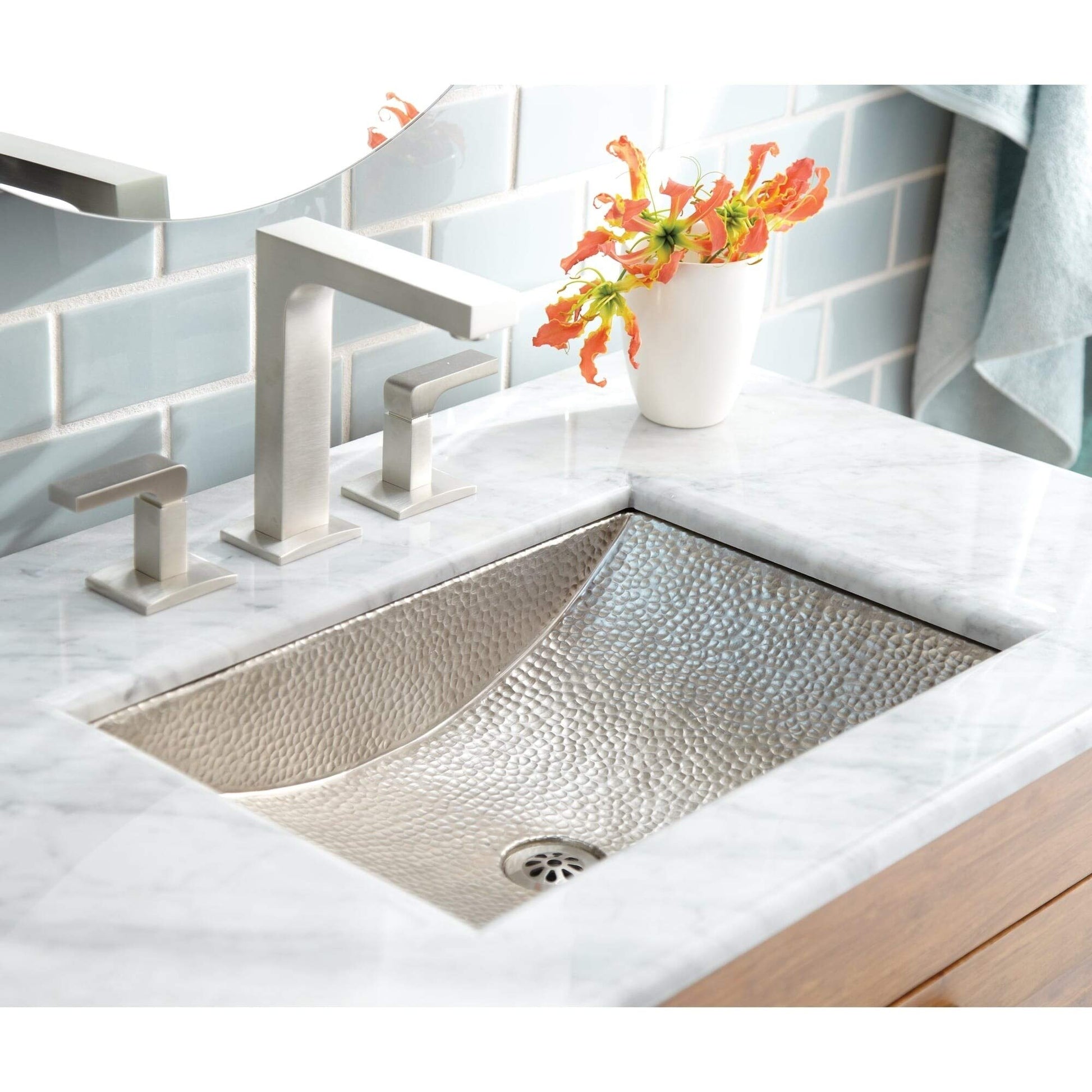 Hammered copper rectangular undermount sink with textured surface, installed in white marble countertop with brushed nickel f