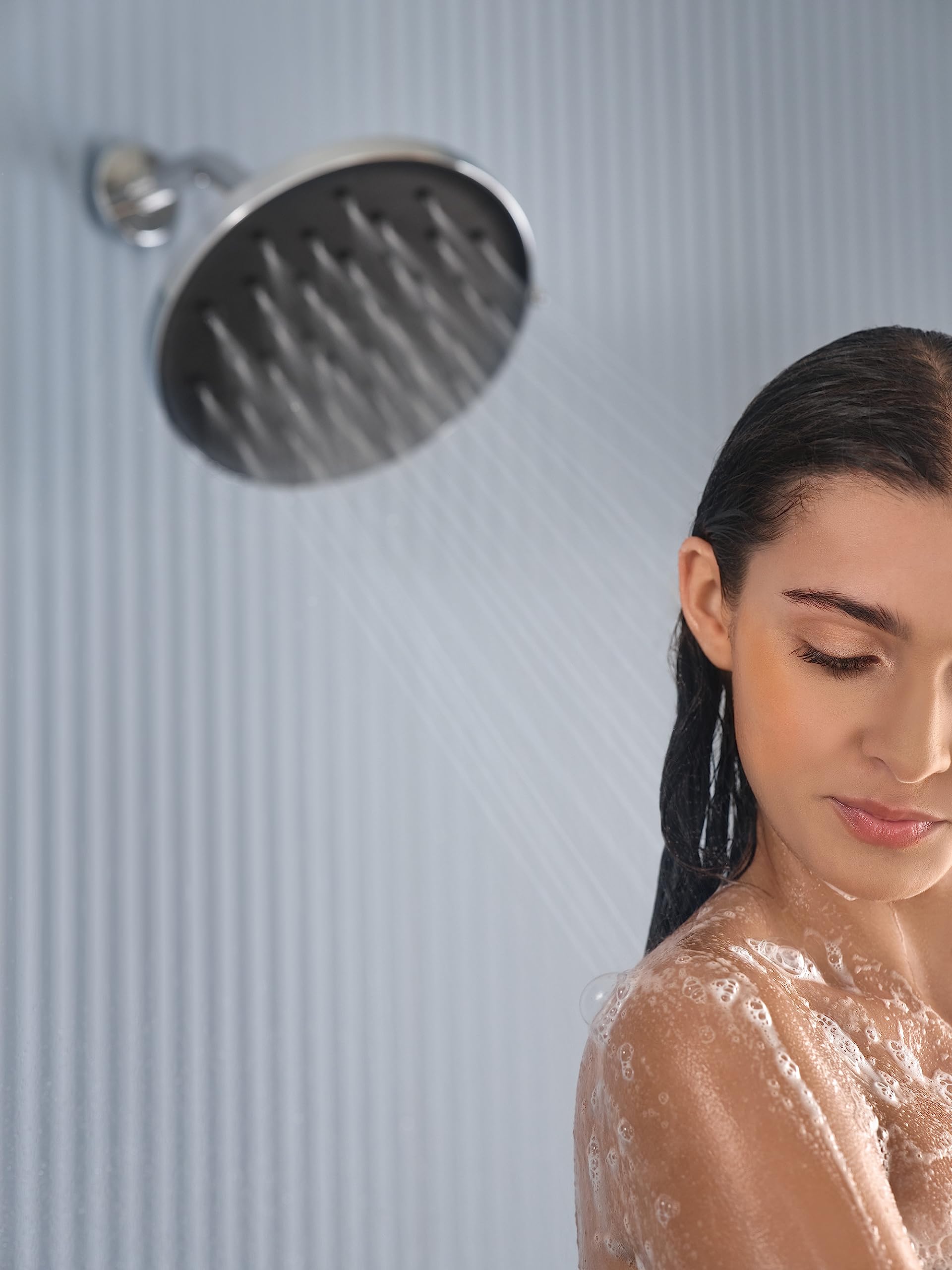Chrome circular rainshower head mounted on wall with a small chrome control valve above it.