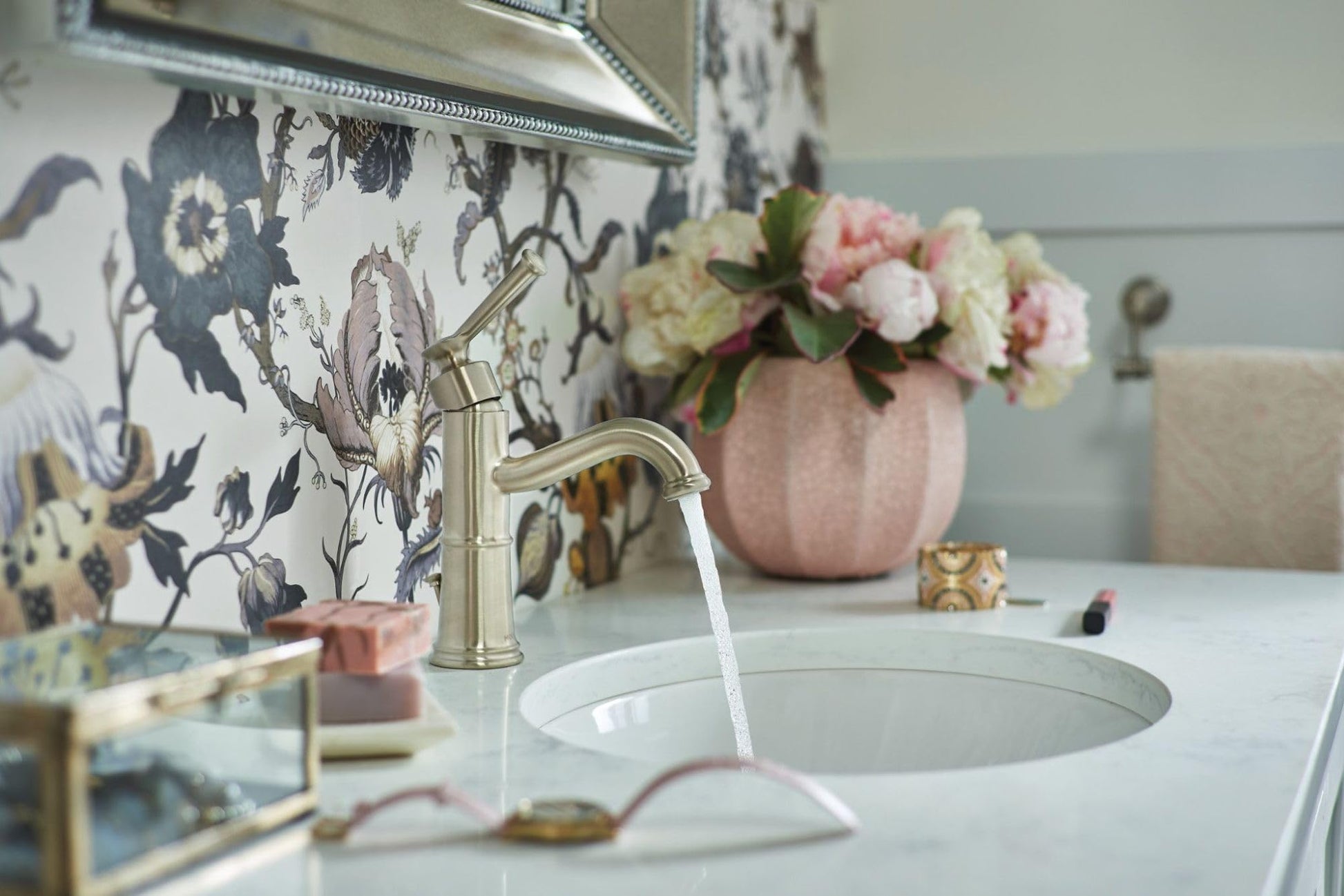 Brushed nickel single-handle bathroom faucet with curved spout dispensing water into round white sink basin.