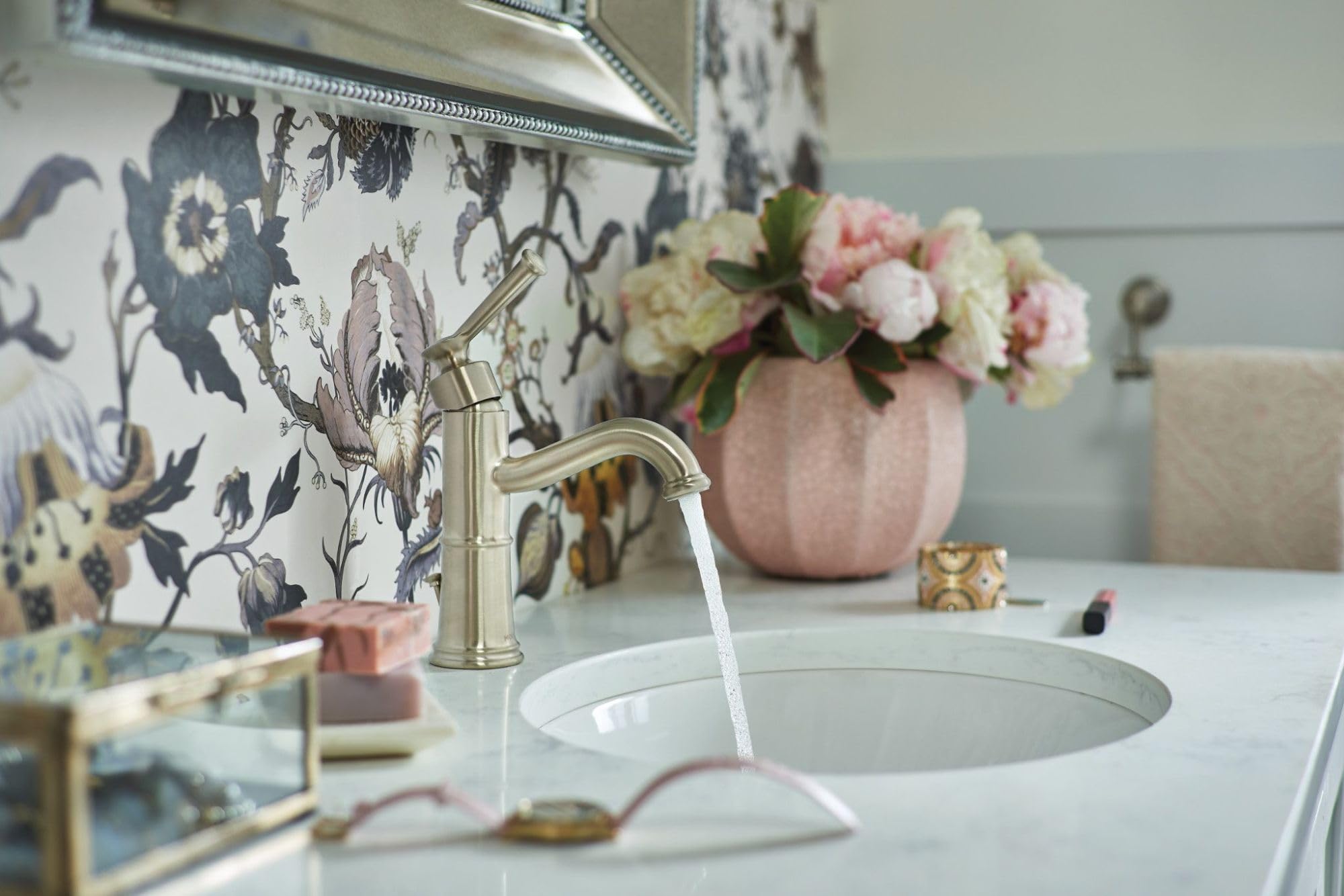 Brushed nickel single-handle bathroom faucet with curved spout dispensing water into round white sink basin.