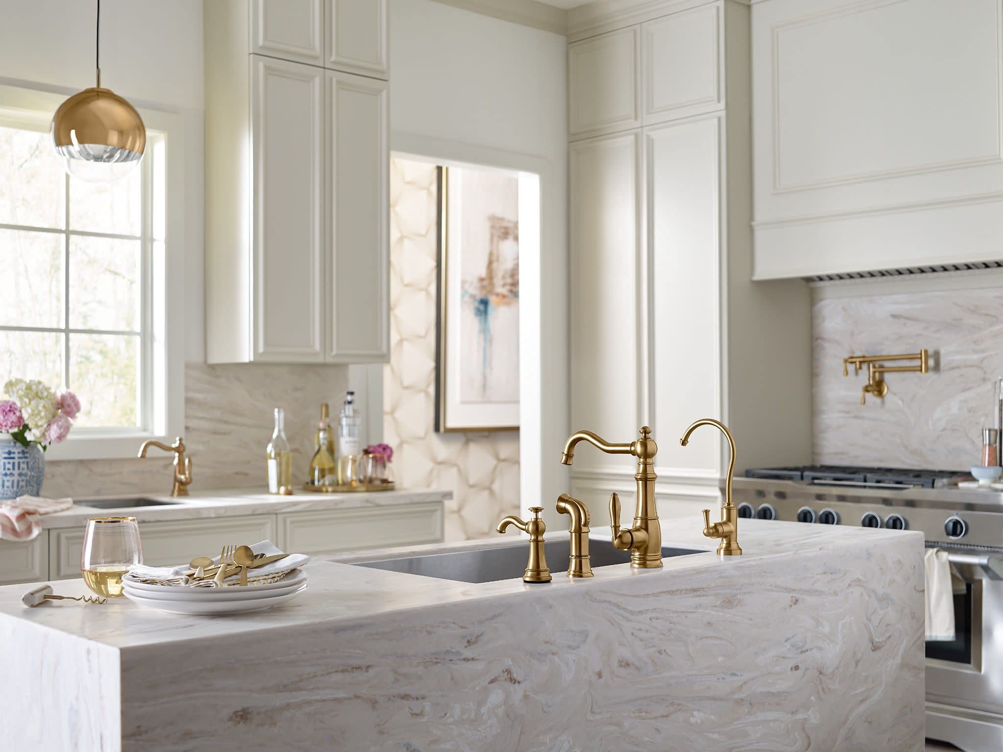 Brushed gold traditional pot filler faucet mounted on white marble kitchen island backsplash.