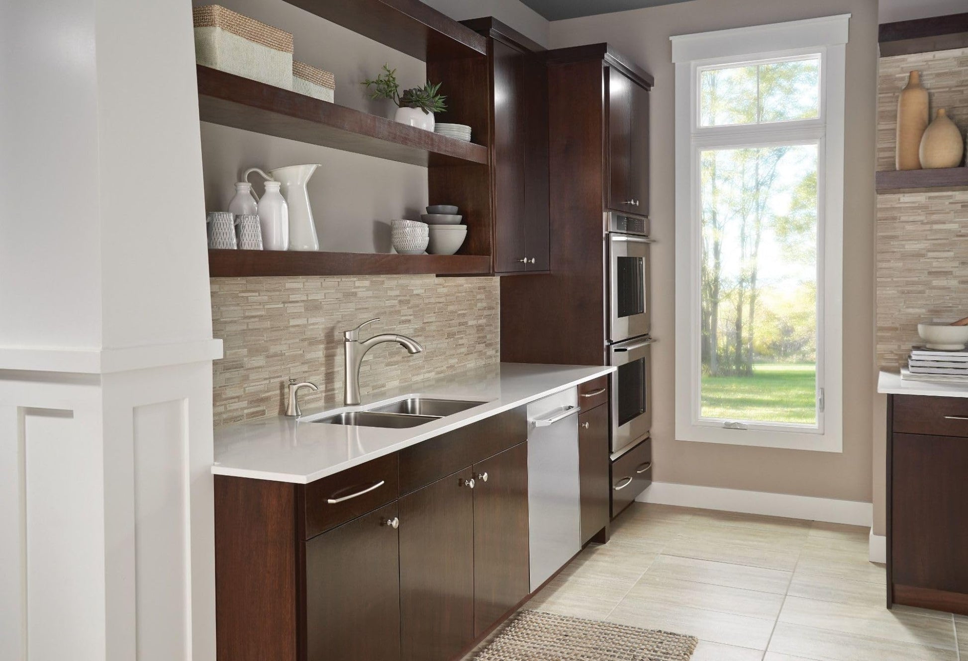 Stainless steel deck-mounted kitchen soap dispenser with curved spout installed on kitchen counter next to sink.