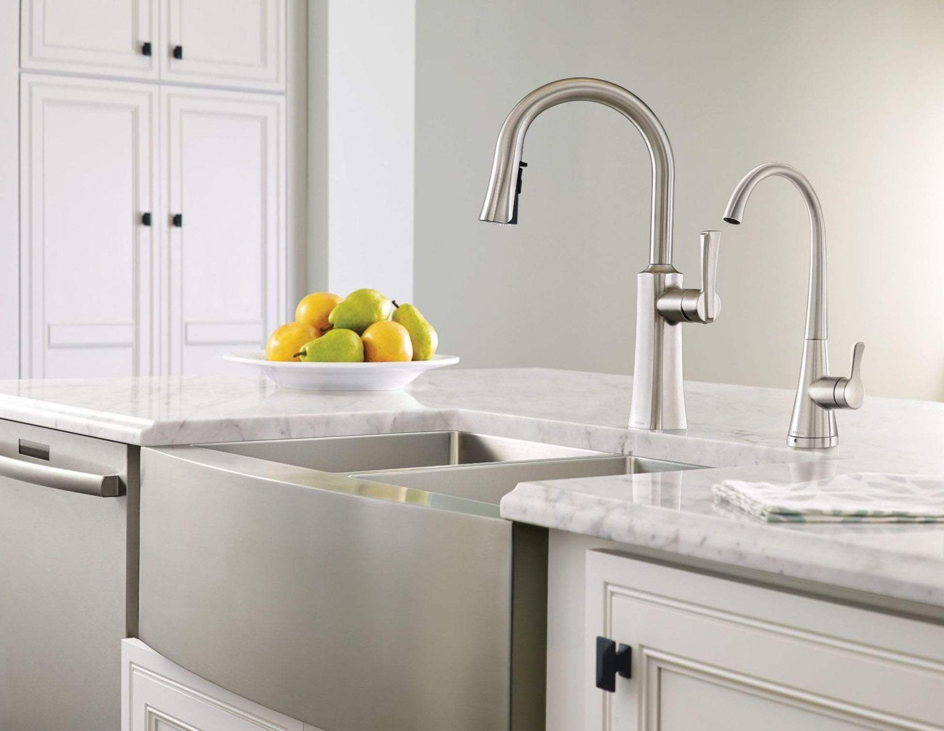Satin stainless steel double-bowl farmhouse apron front sink installed in white kitchen countertop with two faucets.