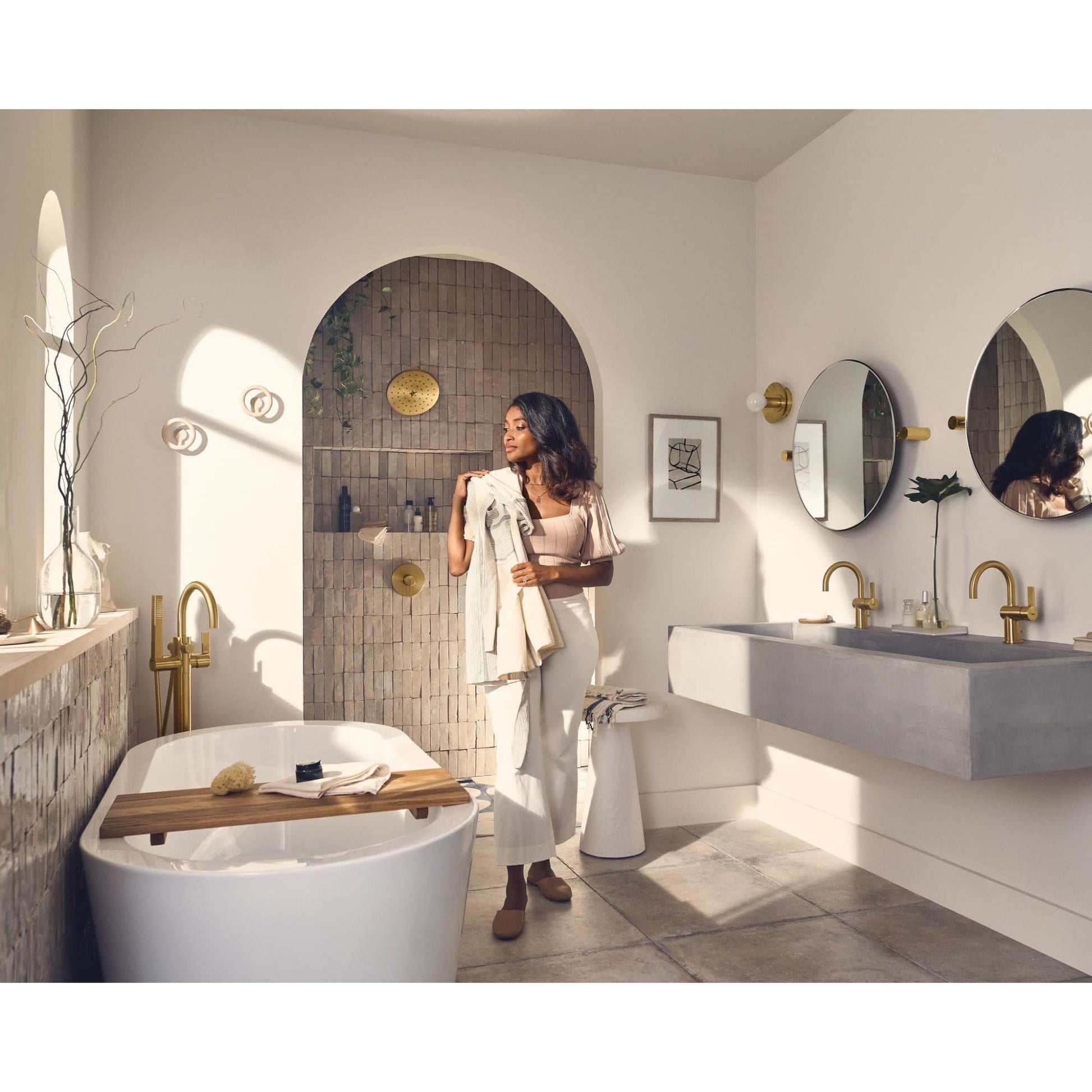 Brushed nickel freestanding tub filler with single handle and attached handheld showerhead positioned next to white soaking t
