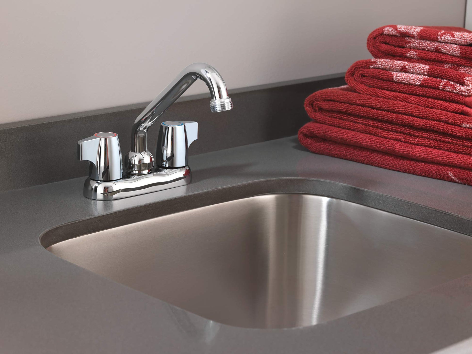 Chrome two-handle laundry faucet with curved spout mounted on dark countertop above stainless steel sink.