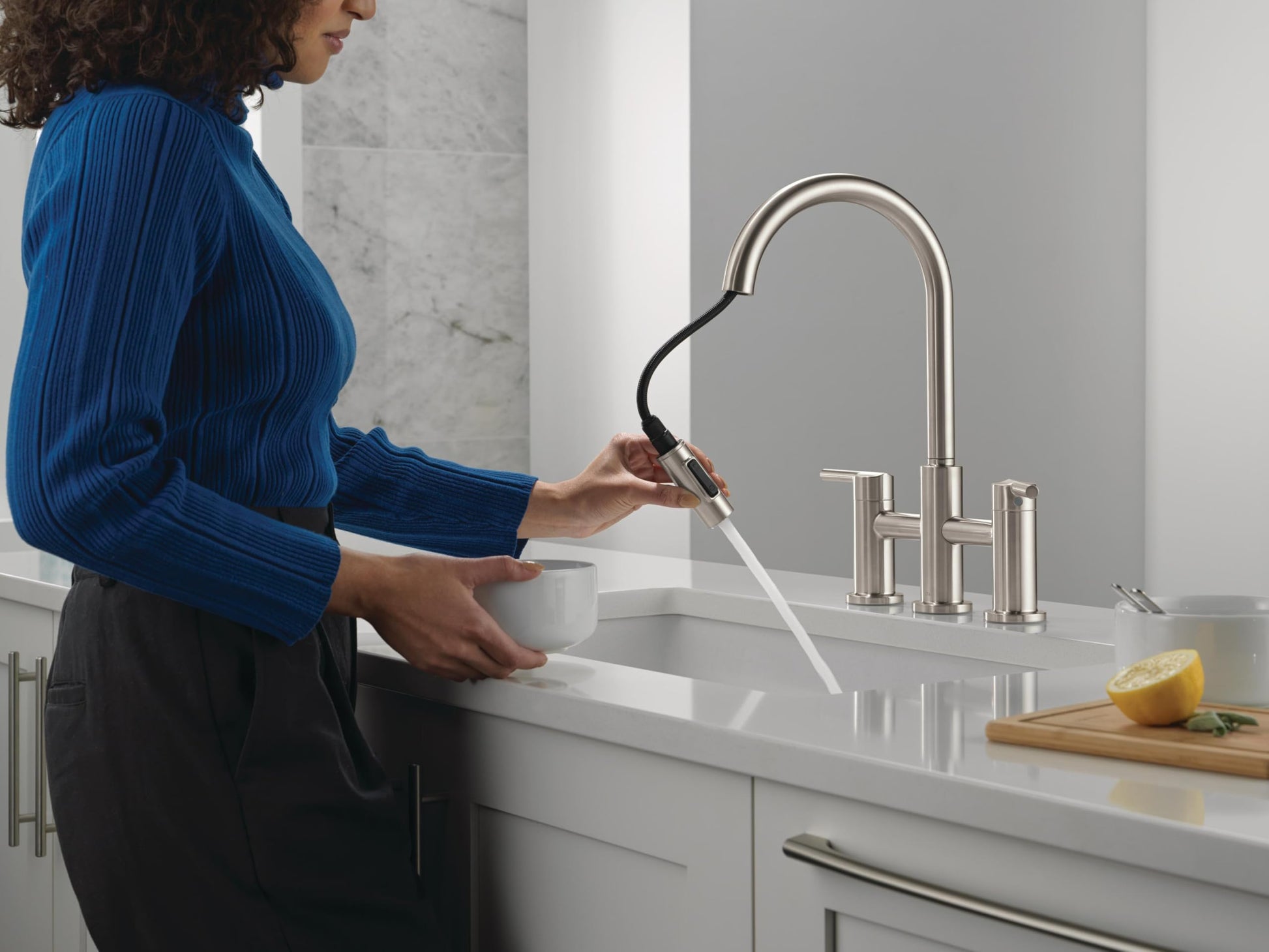 Stainless steel two-handle bridge kitchen faucet with pull-down sprayer, shown installed at sink with spray extended.