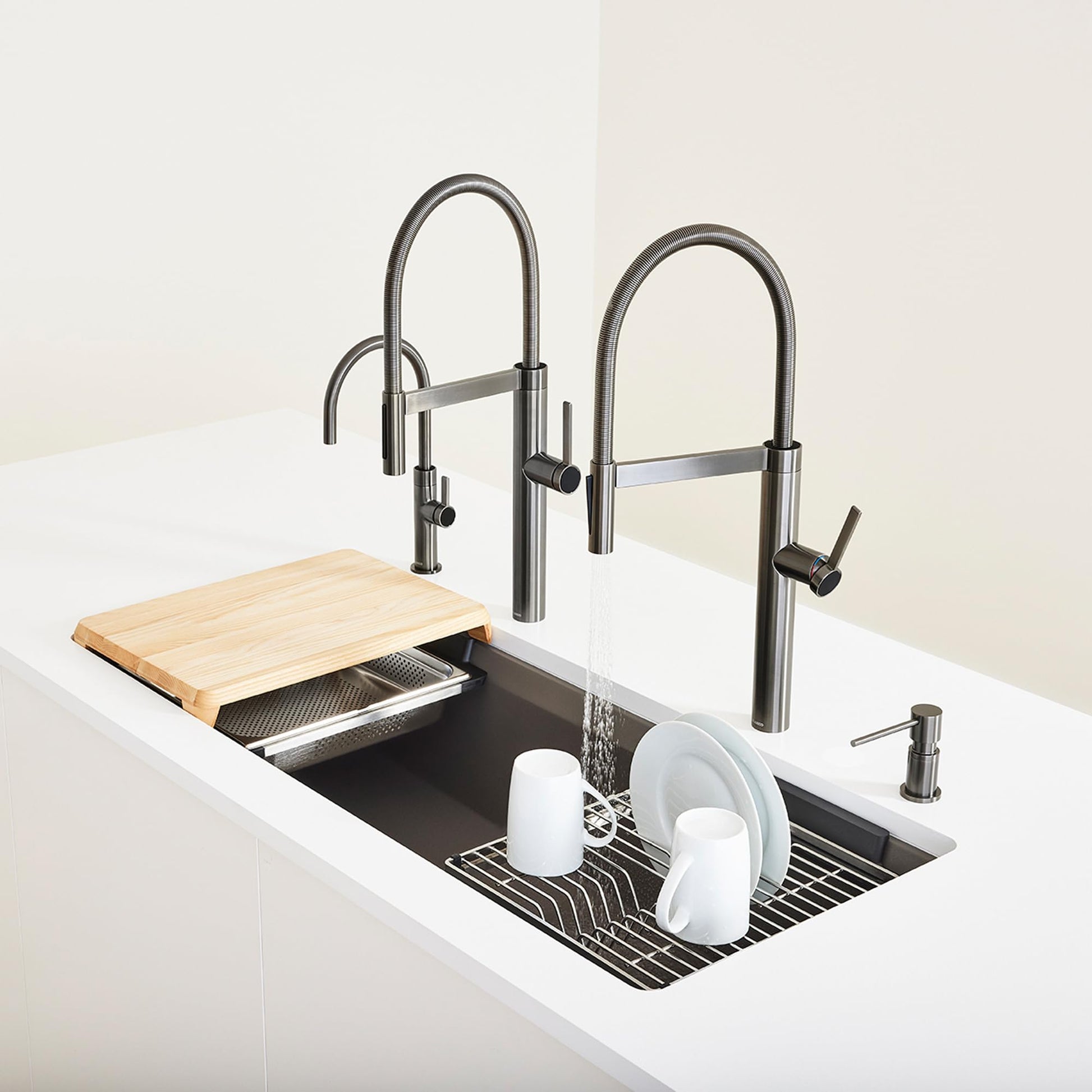 Stainless steel dish rack with grid pattern insert, wooden cutting board, and white dishes in workstation sink with dual fauc