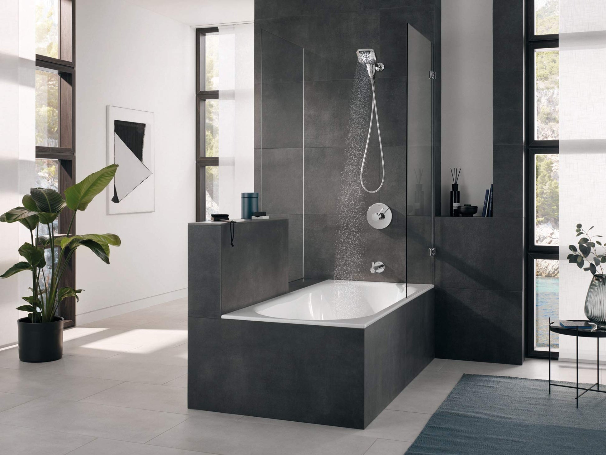 Chrome hand shower with square showerhead mounted on dark tile shower wall above bathtub.