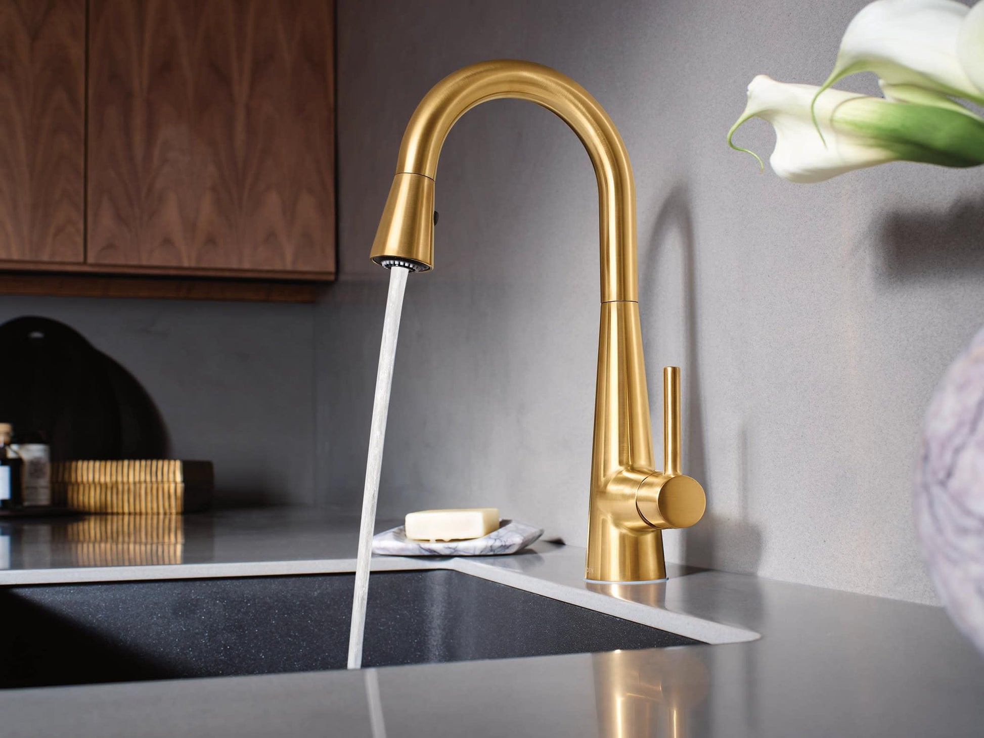Brushed gold pulldown faucet with high arc spout and single handle mounted above dark sink basin.
