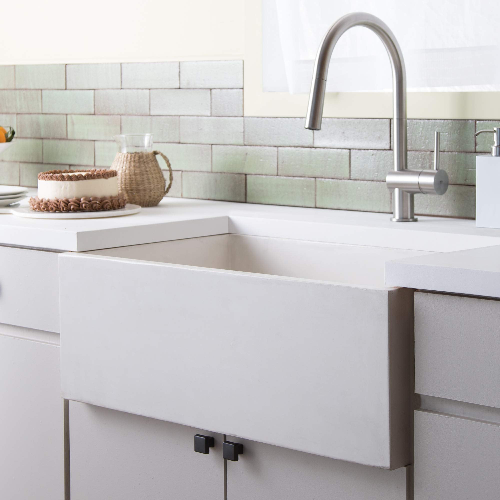 White farmhouse sink with high-arc stainless steel faucet in kitchen with subway tile backsplash.