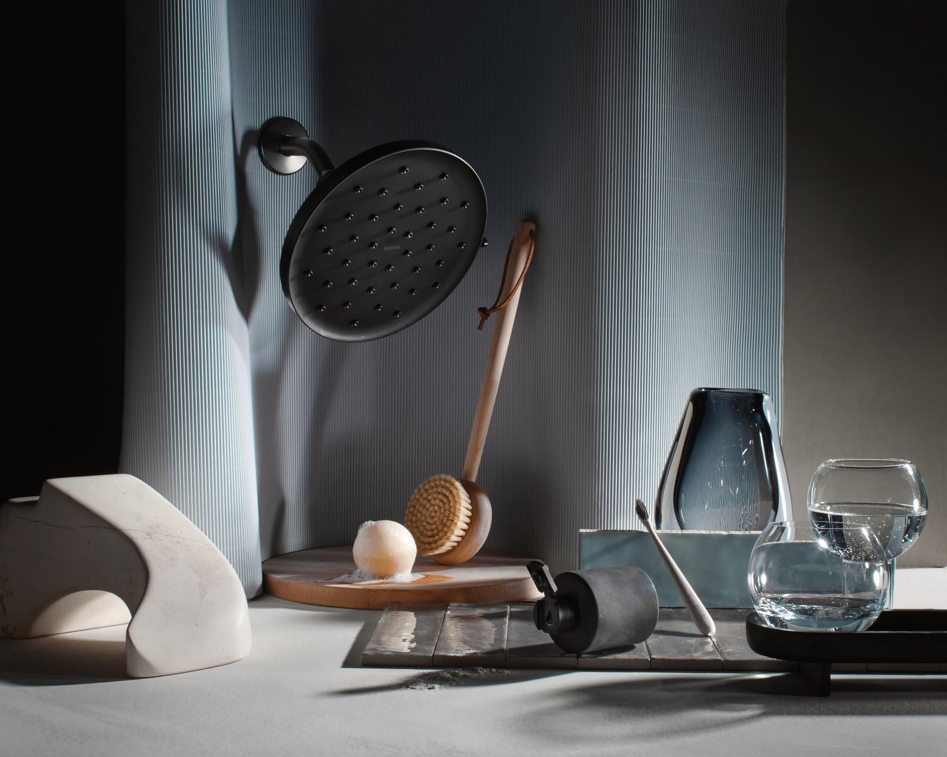 Matte black circular rainshower head with multiple spray holes mounted on wall with adjustable arm.