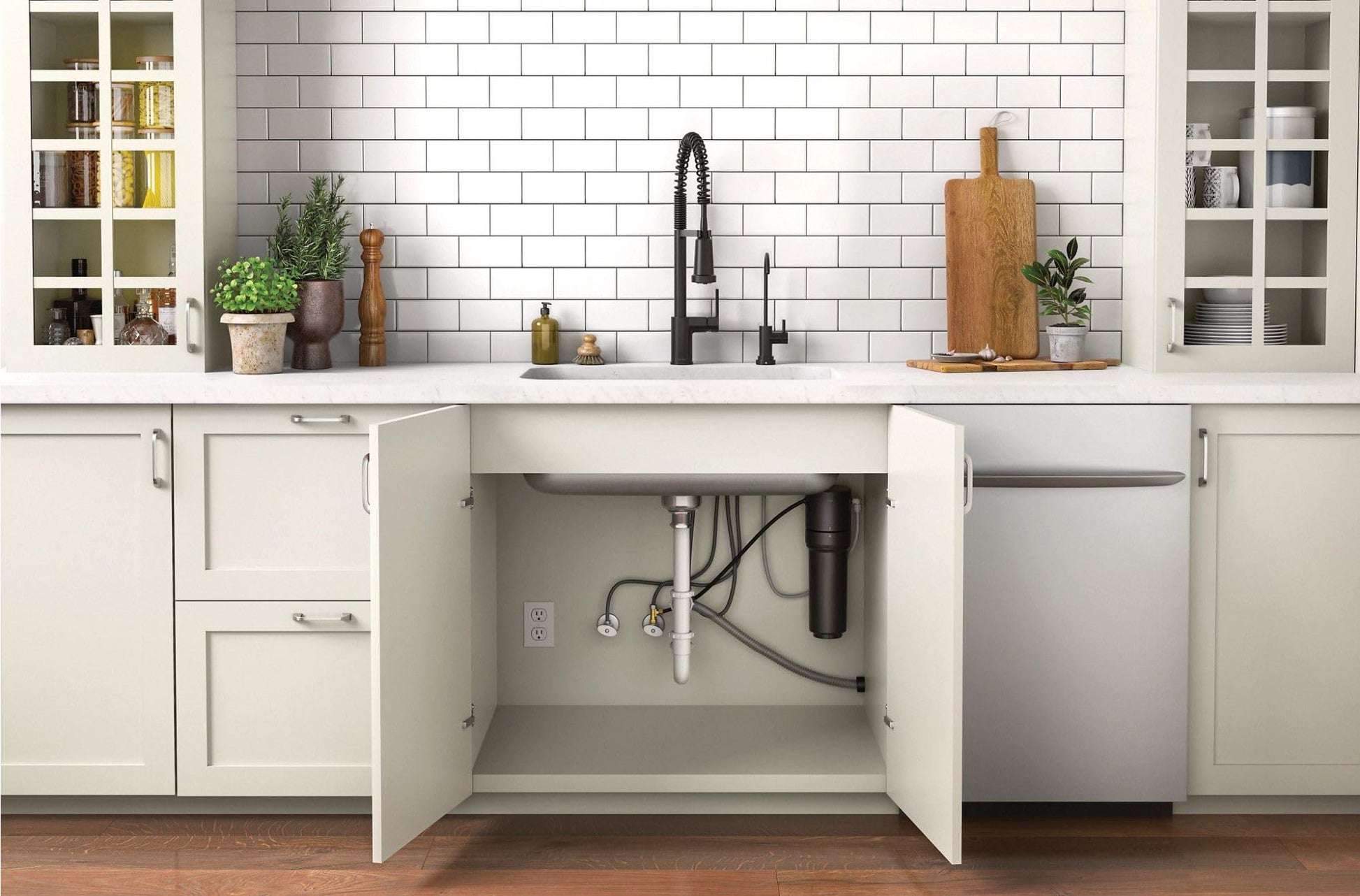 Chrome under-sink water filtration system installed beneath kitchen sink with white cabinets and black faucet.