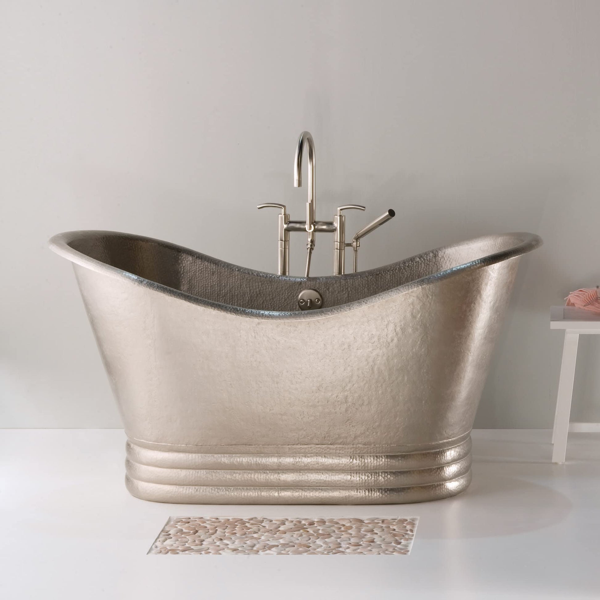 Hammered copper freestanding bathtub with curved sides, chrome faucet and handheld showerhead mounted on rim.