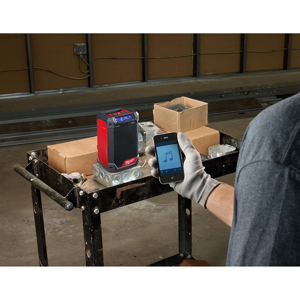 Milwaukee M12 compact radio with red and black housing and digital display on work table.