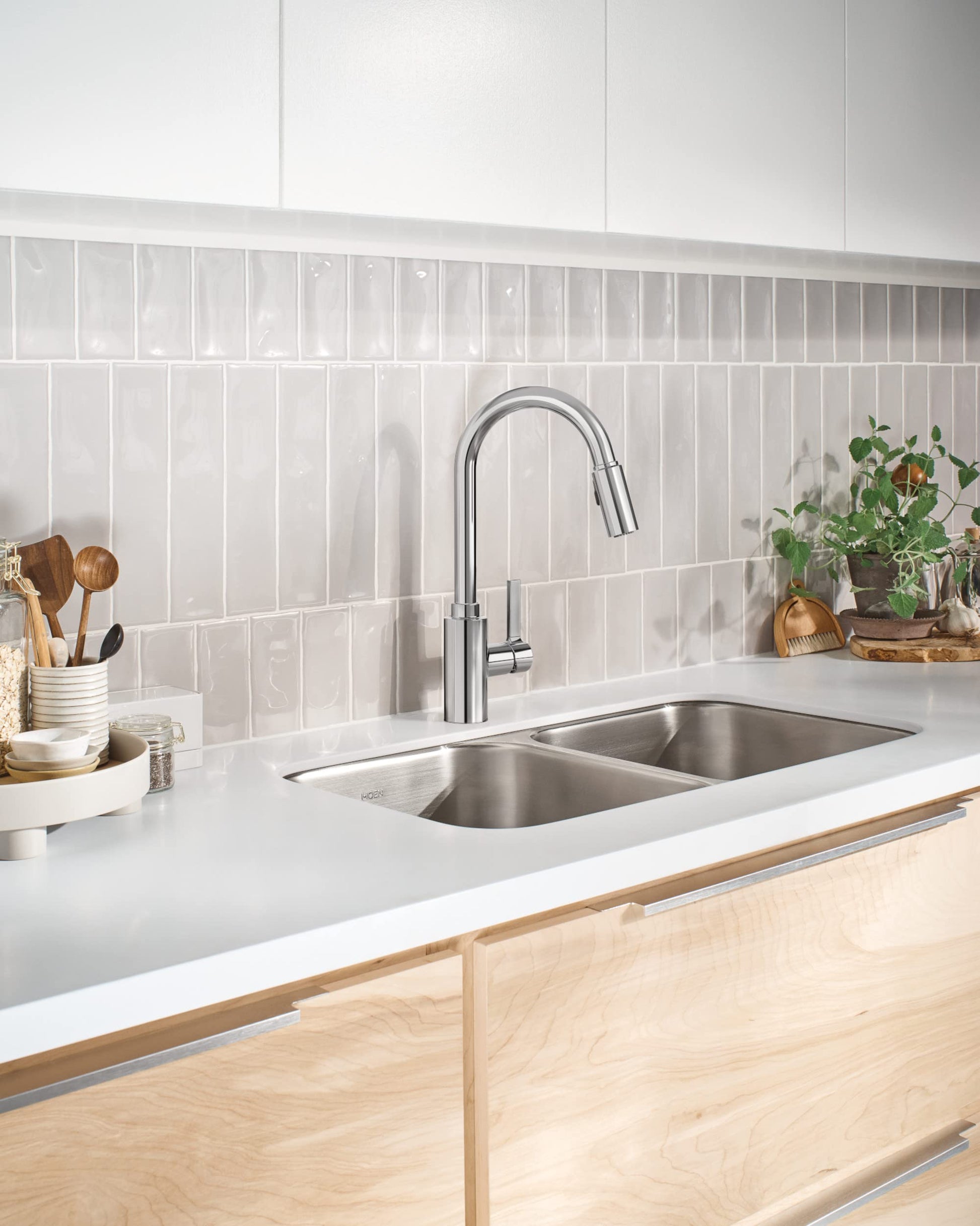 Chrome kitchen faucet with pull-down sprayer mounted above double stainless steel sink in white countertop.