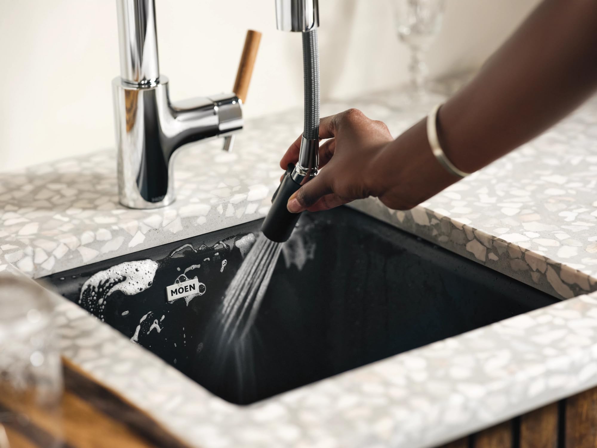 Chrome bar faucet with pulldown spray head and wood handle being used at a black undermount sink.