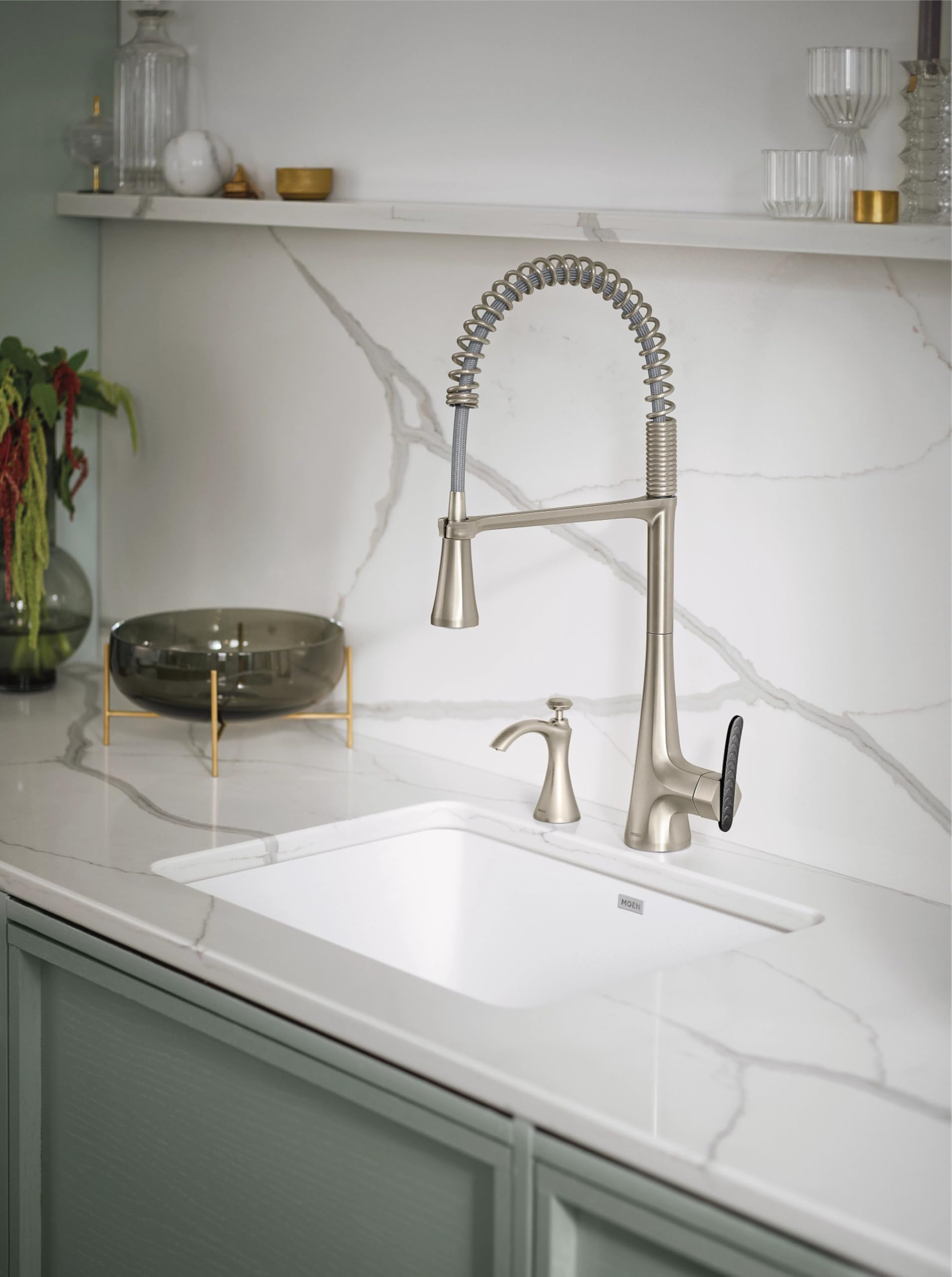 Stainless steel pulldown kitchen faucet with coiled hose and single handle installed above white sink on marble countertop.