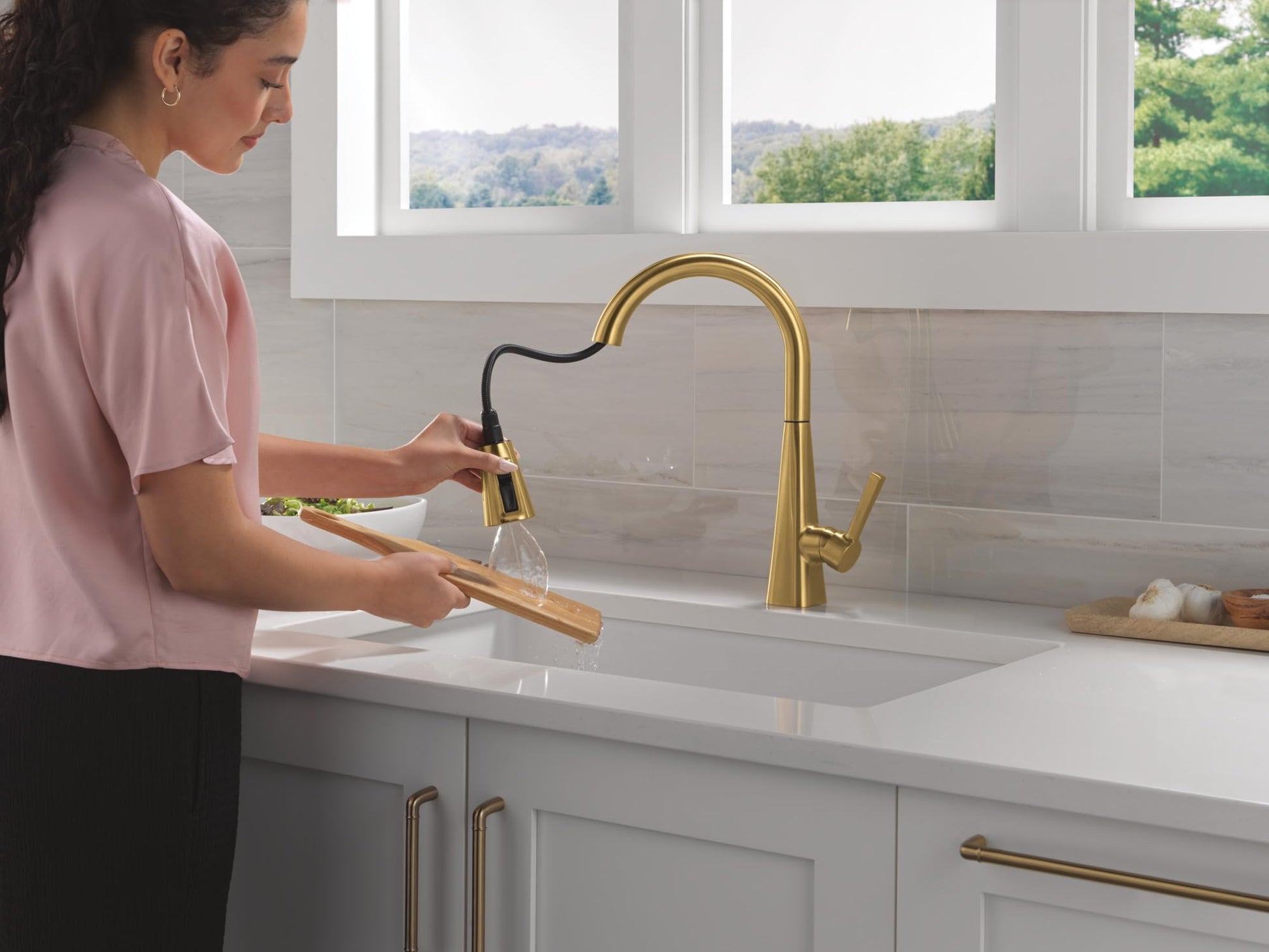 Brushed gold single-handle pull-down kitchen faucet with curved spout shown installed above white sink.