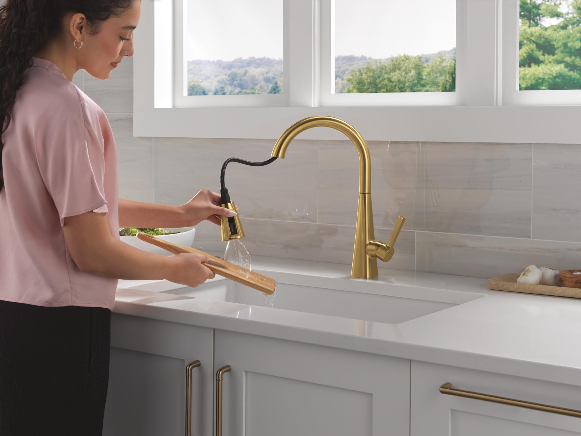 Brushed gold single-handle pull-down kitchen faucet with curved spout shown installed above white sink.